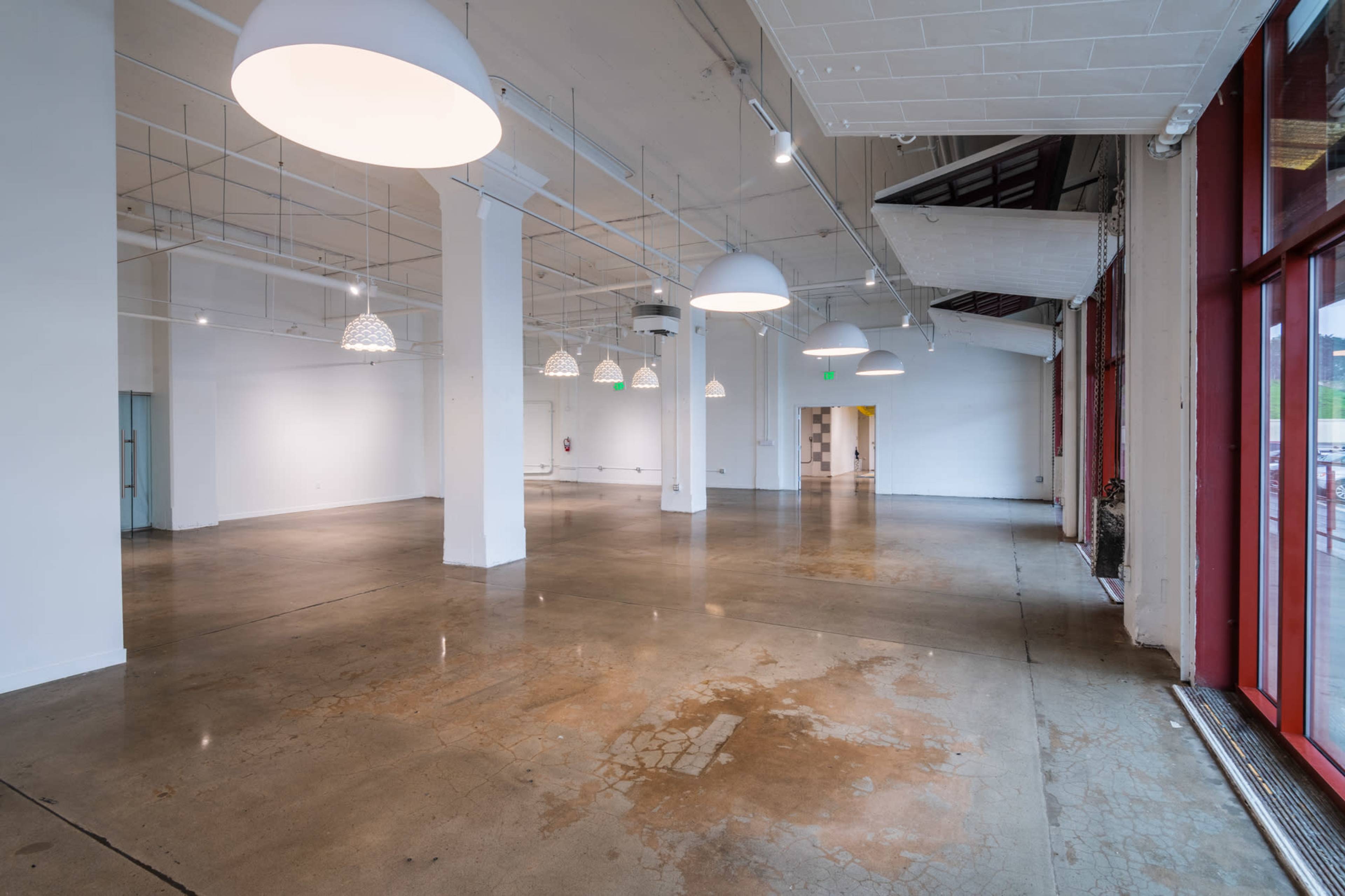 A spacious, empty interior with polished concrete floors and several pendant lights hanging from the ceiling.