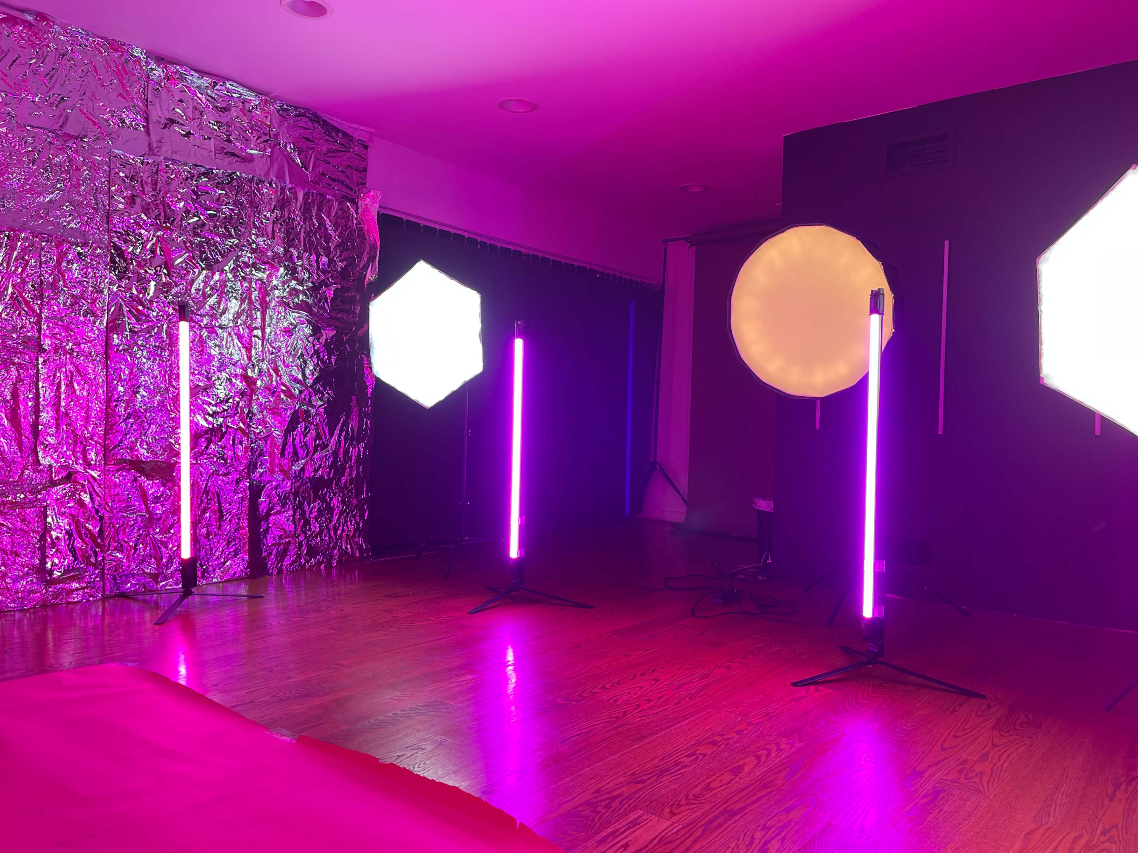 A photography studio setup with various light sources, including tall, colored lights and softboxes, arranged around a wooden floor.