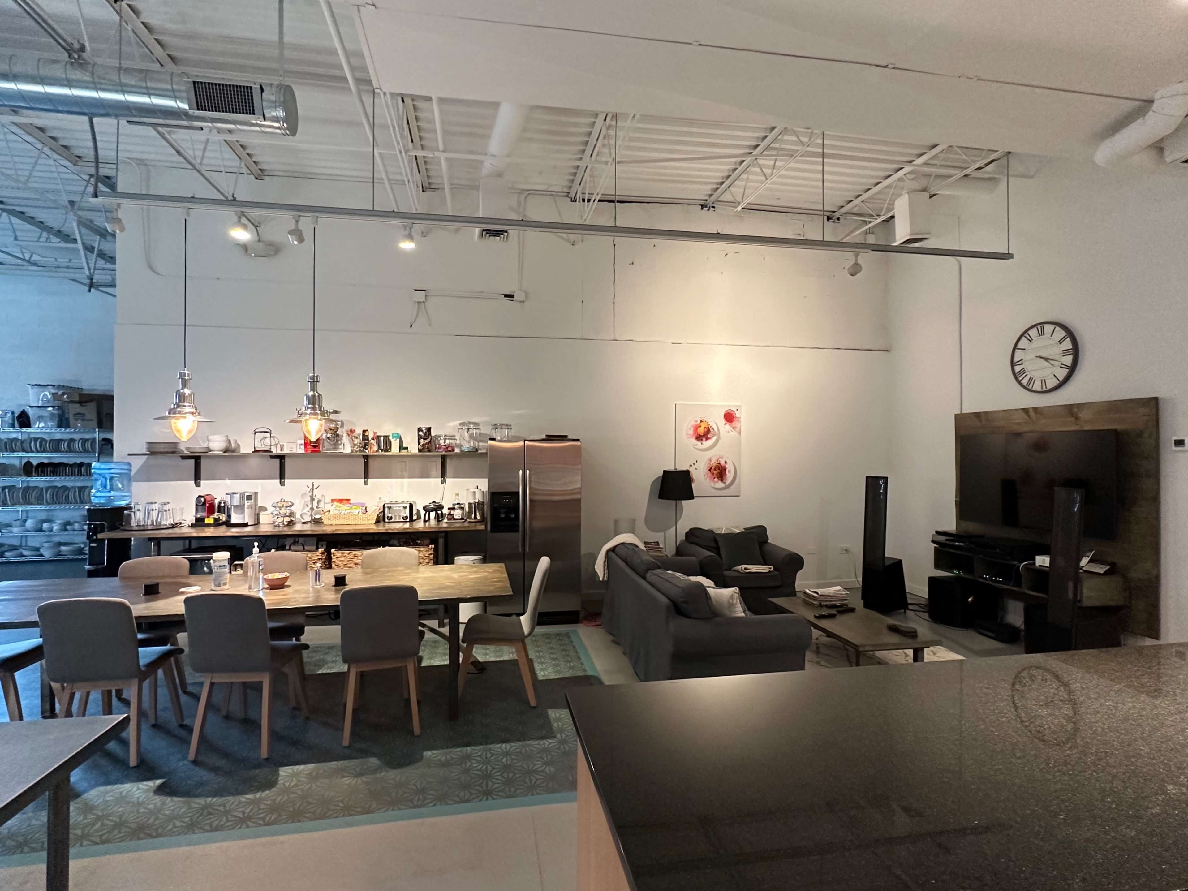 A modern open-concept kitchen and dining area with a large table, a sofa, and various kitchen appliances visible on shelves.