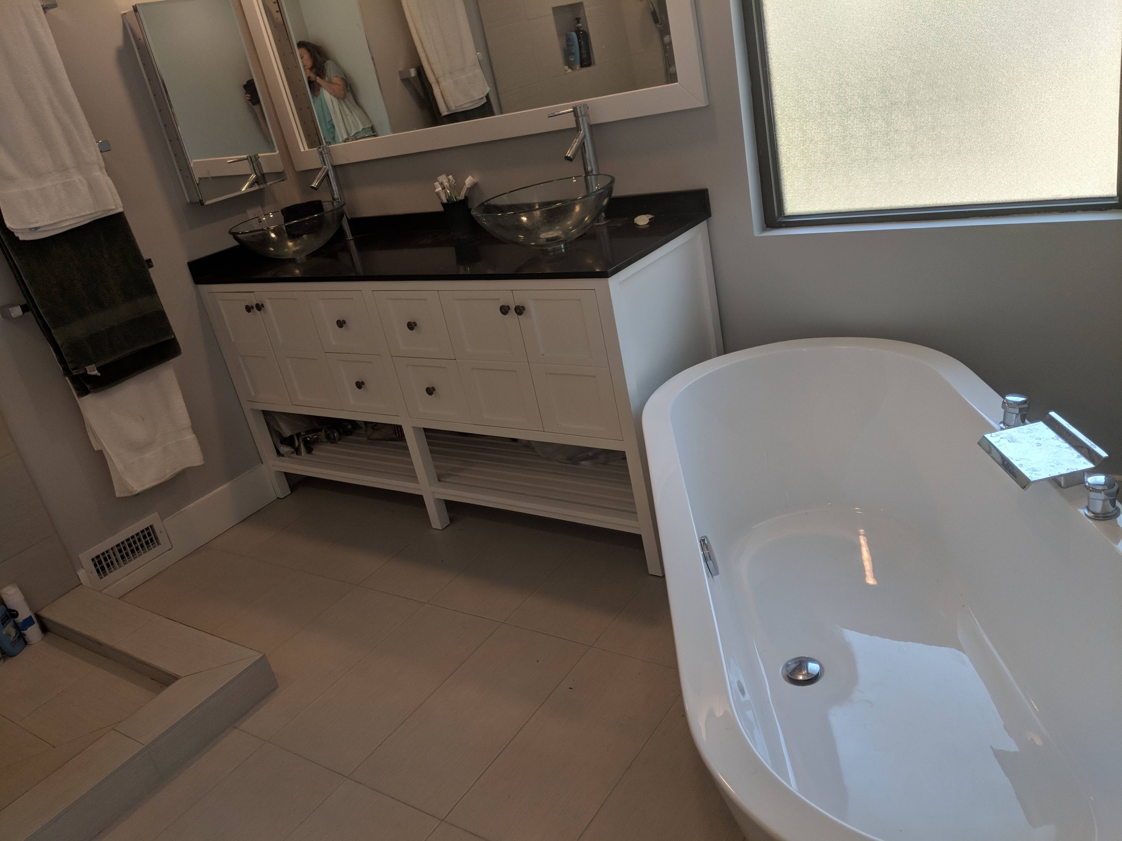 A modern bathroom featuring a freestanding bathtub, dual sinks with glass bowls, a white vanity with storage, and a large window.
