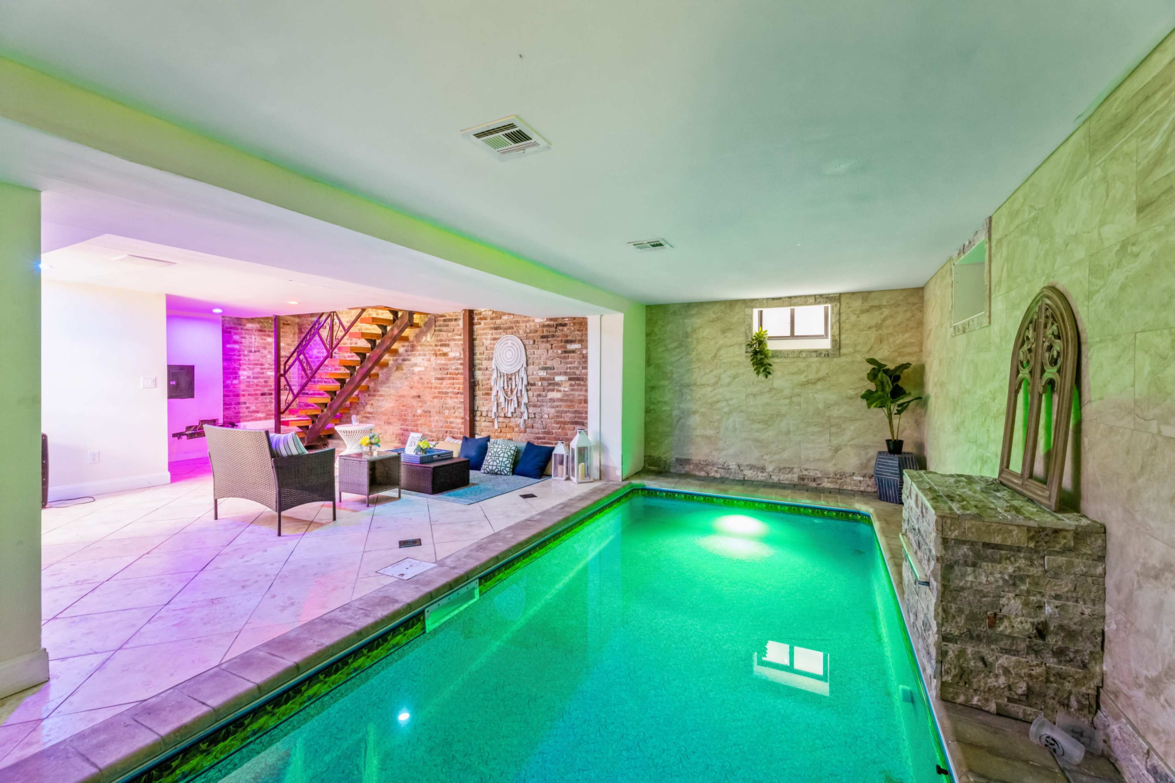 An indoor pool area with green water, adjacent to a seating area featuring colorful lighting and a staircase in the background.