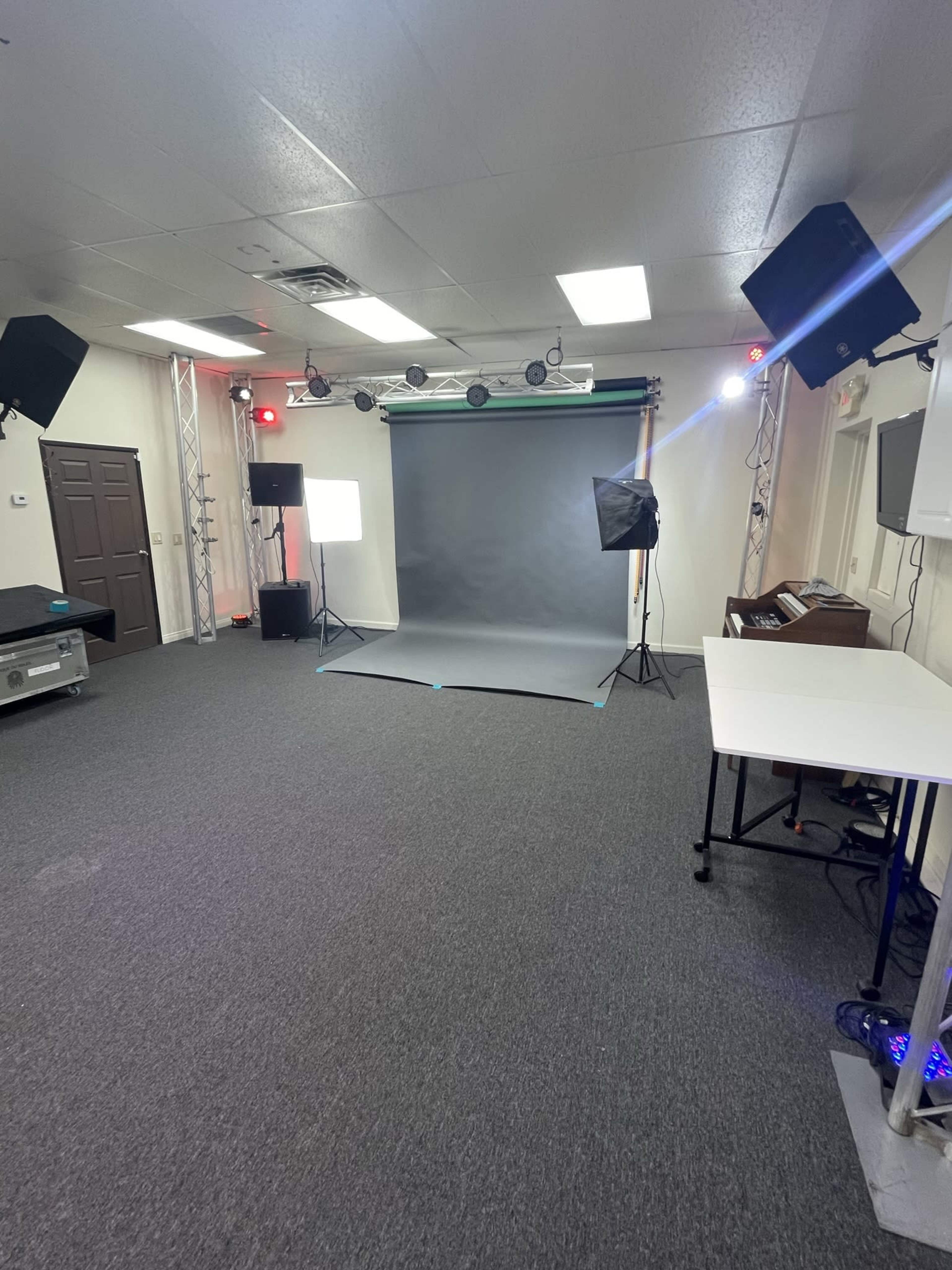 An empty photo studio with a gray backdrop, lighting equipment, and a table.