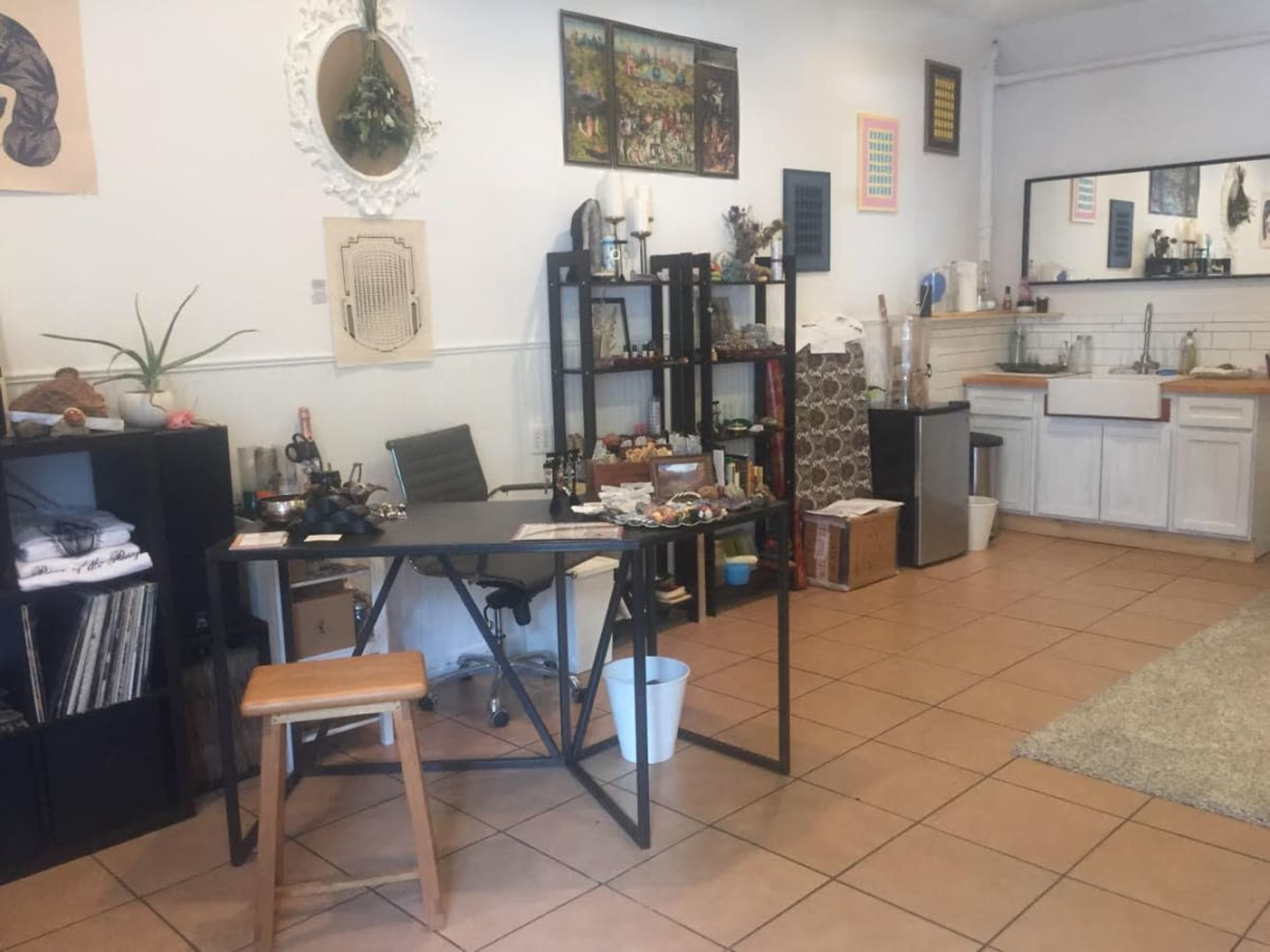 A tidy, well-lit room featuring a desk, shelves with various items, and a small kitchenette area.