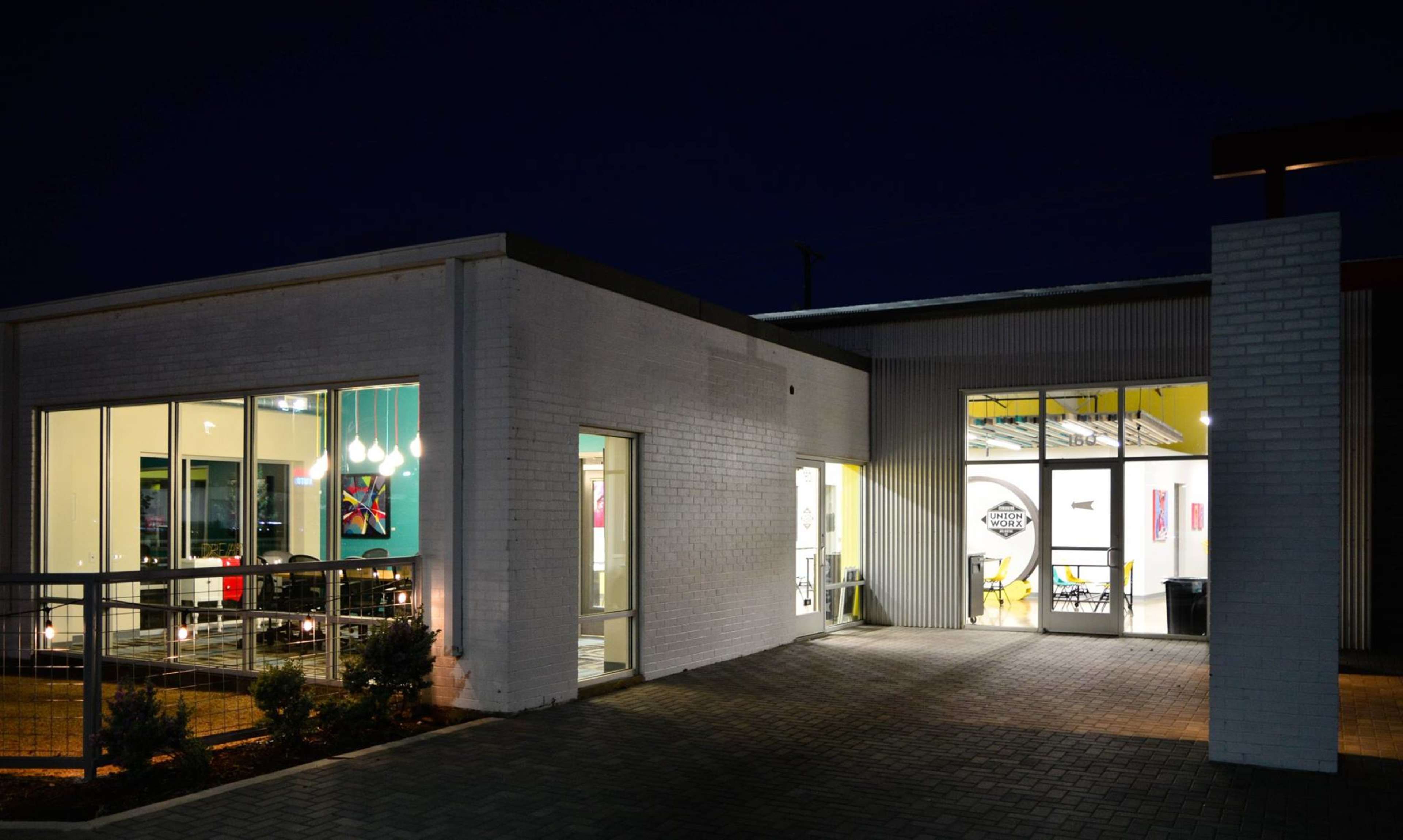 A modern building with large windows and a combination of brick and metal siding is illuminated at night.