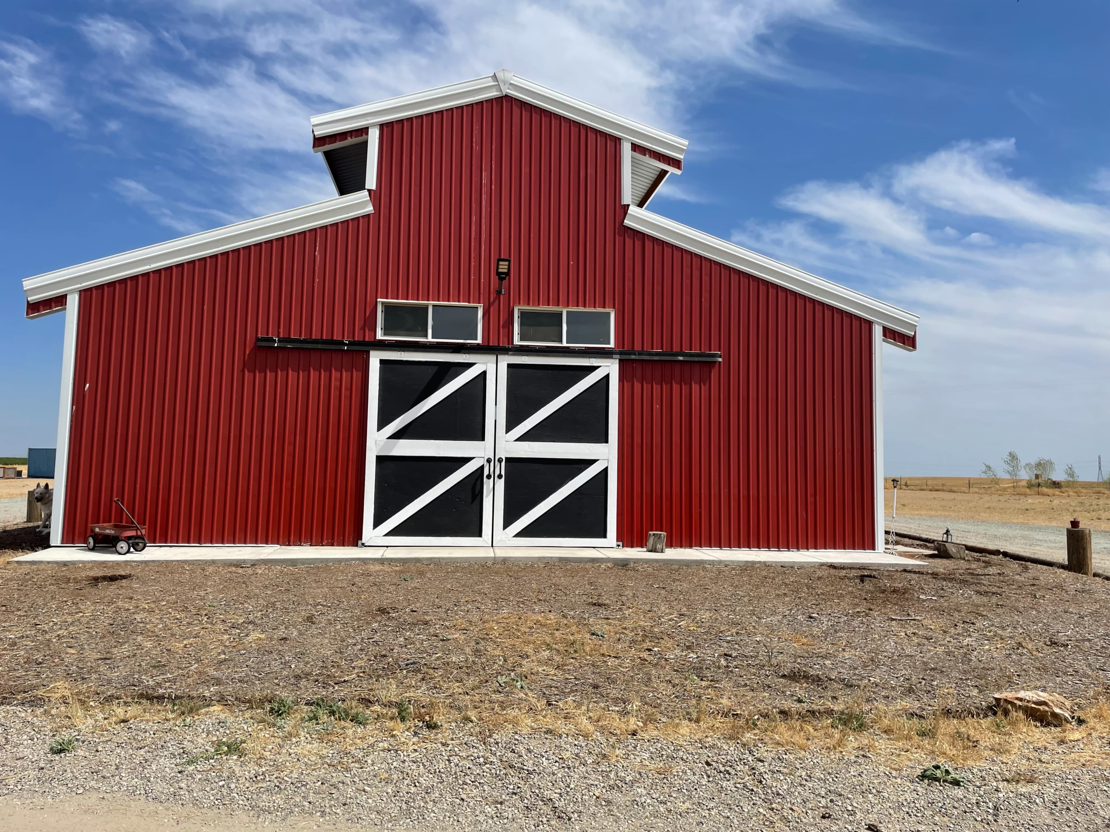 A large red barn with a white door structure, situated in a dry, open landscape.