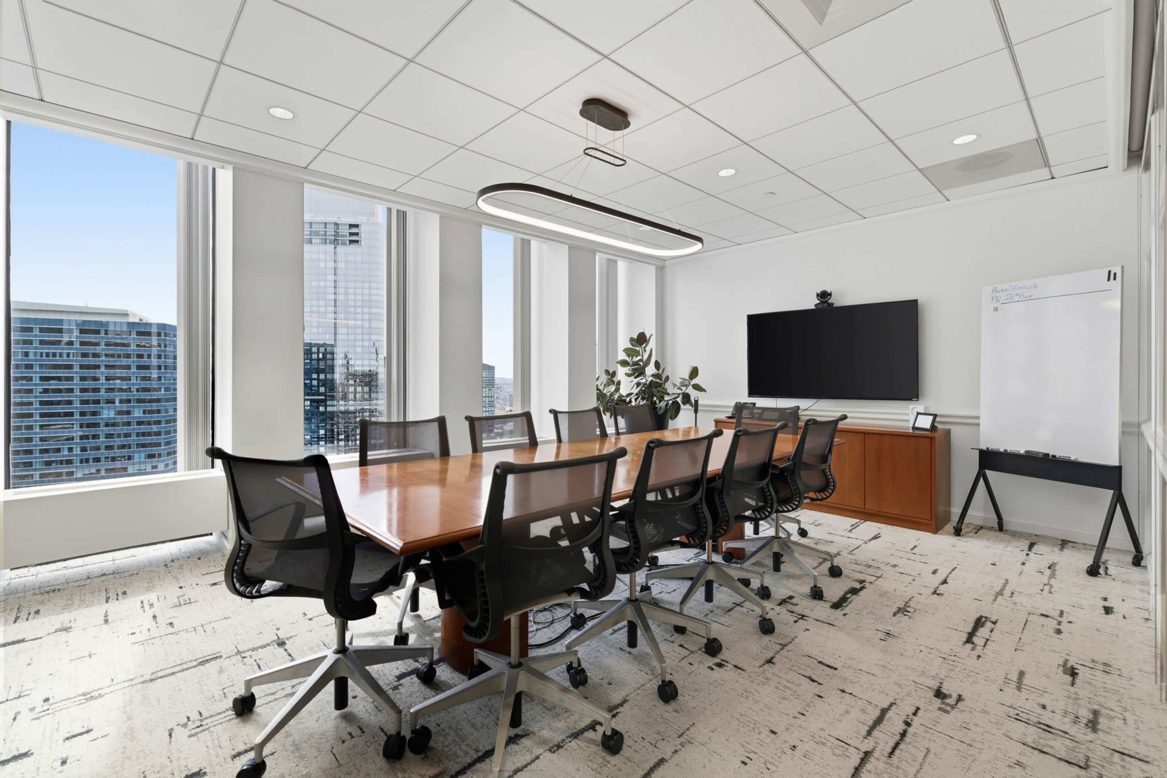A modern conference room features a large wooden table surrounded by ergonomic chairs, with floor-to-ceiling windows offering a view of the city skyline.