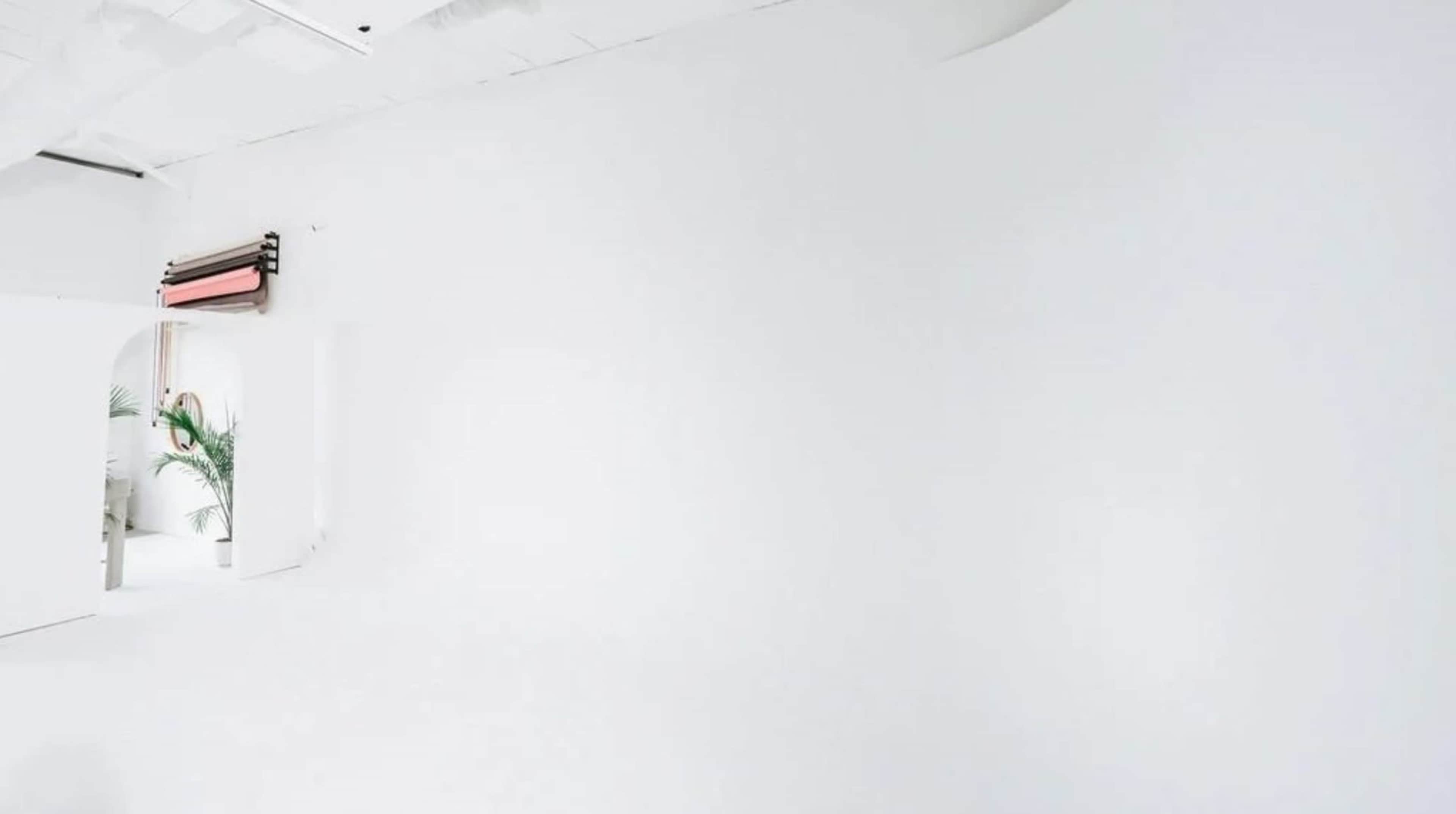 The image shows an empty, minimalist white room with a smooth wall and ceiling.