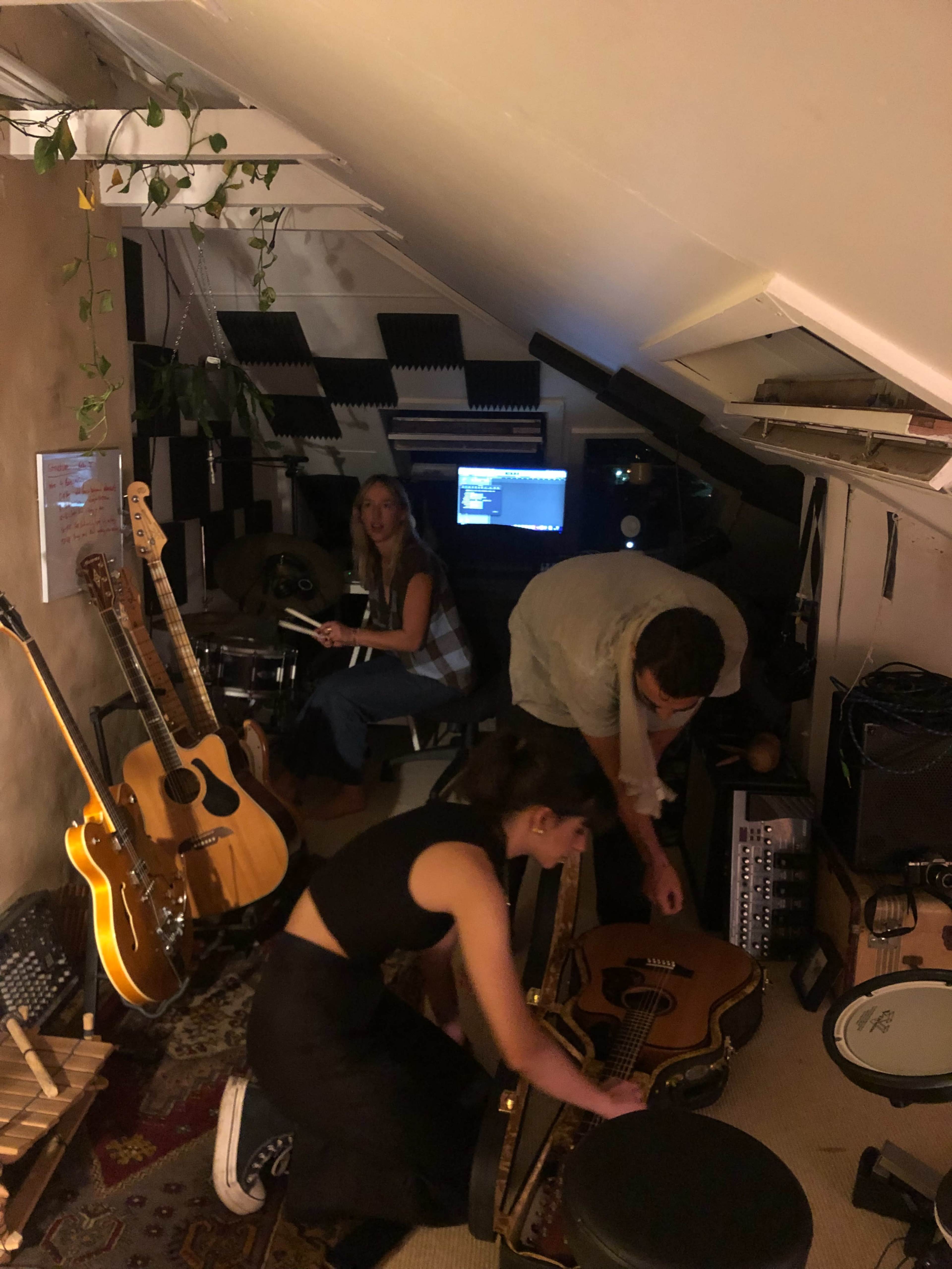 Three people arrange musical instruments in a small recording studio.