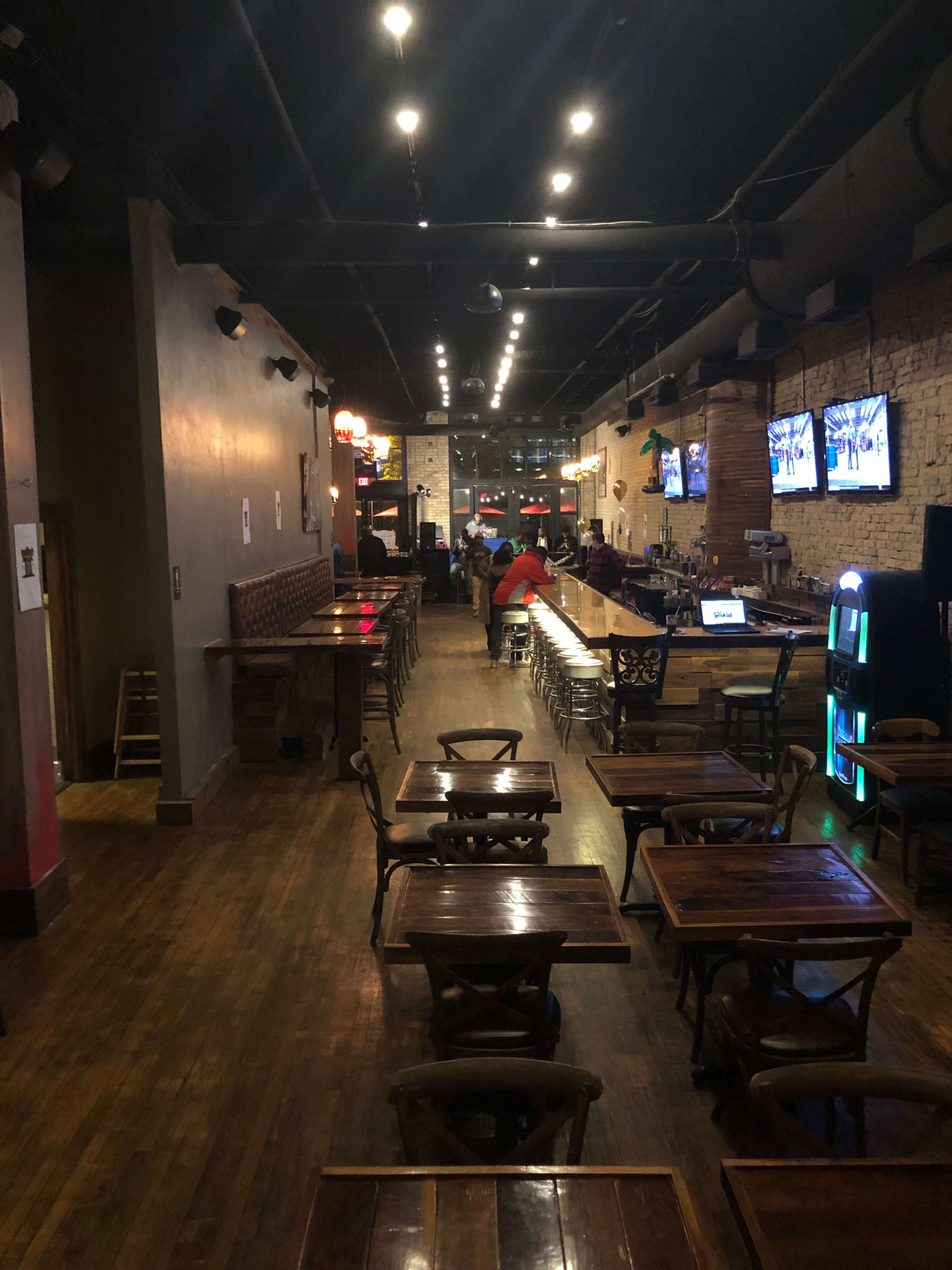 An interior view of a bar or pub with wooden tables, a long counter, and several televisions mounted on the walls.