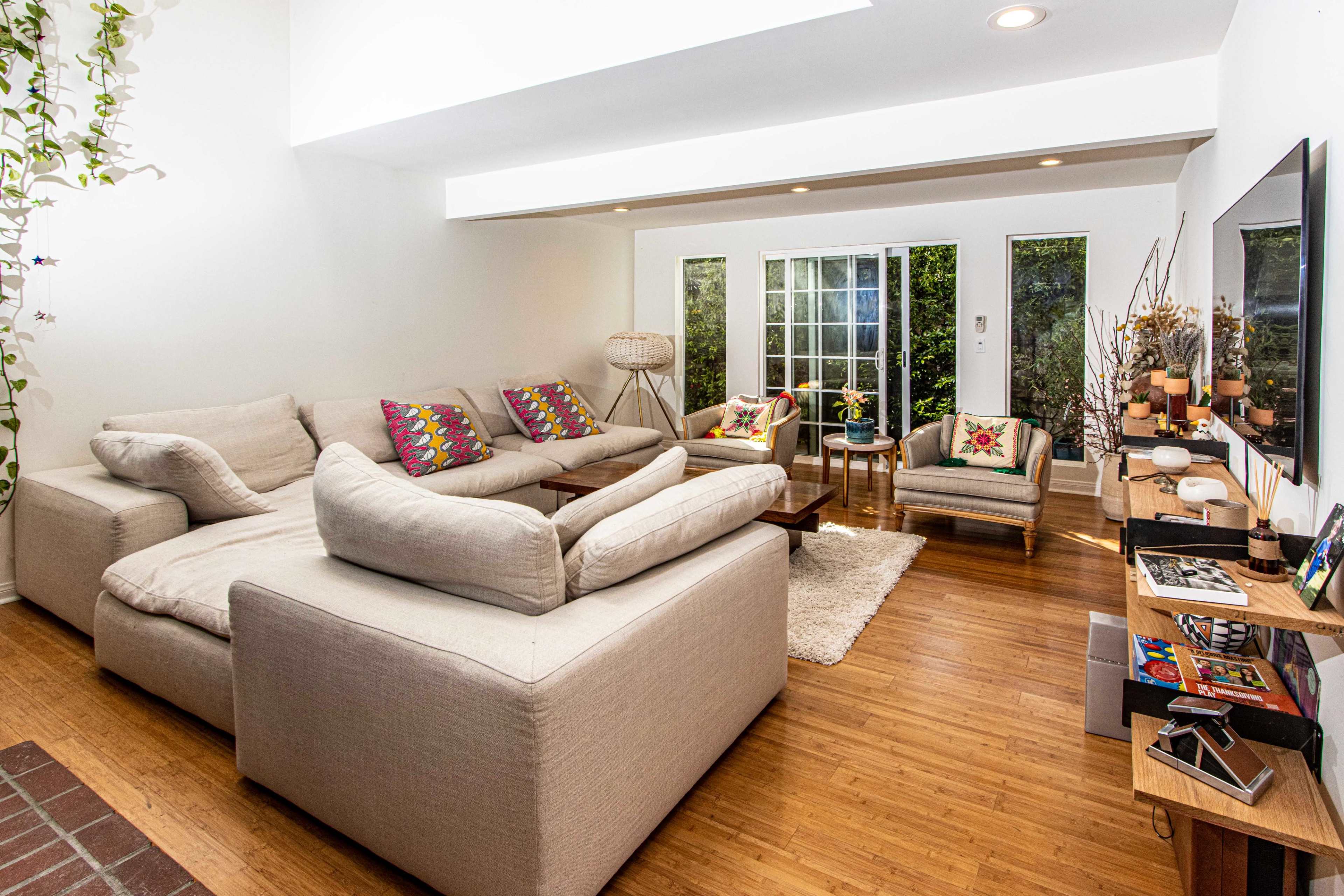 The living room features a large, sectional sofa with decorative pillows, two armchairs, and a coffee table, all arranged around a rug with large windows providing natural light.