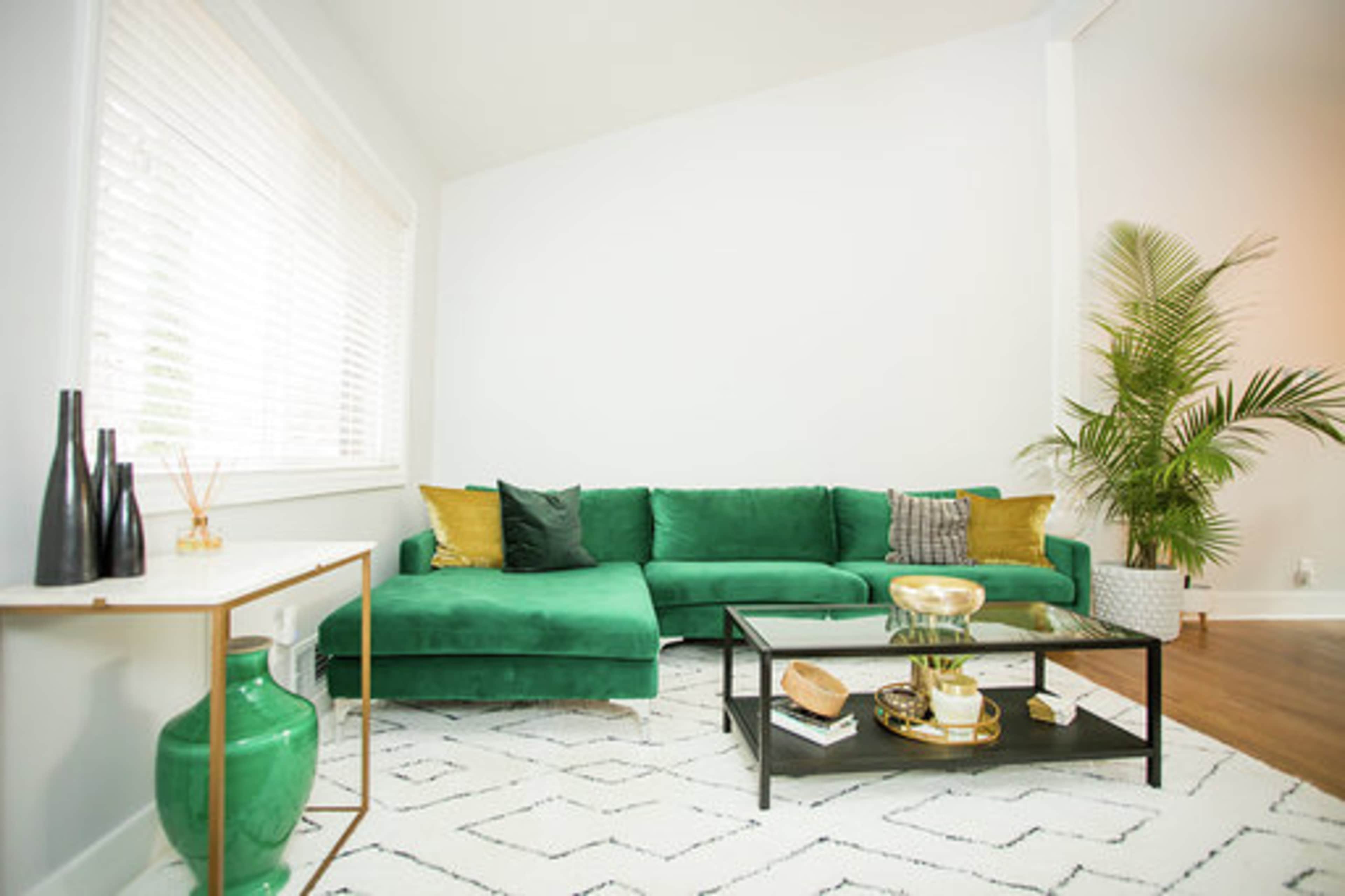 The image shows a modern living room featuring a green sectional sofa, a coffee table with decorative items, and a tall plant in the corner.
