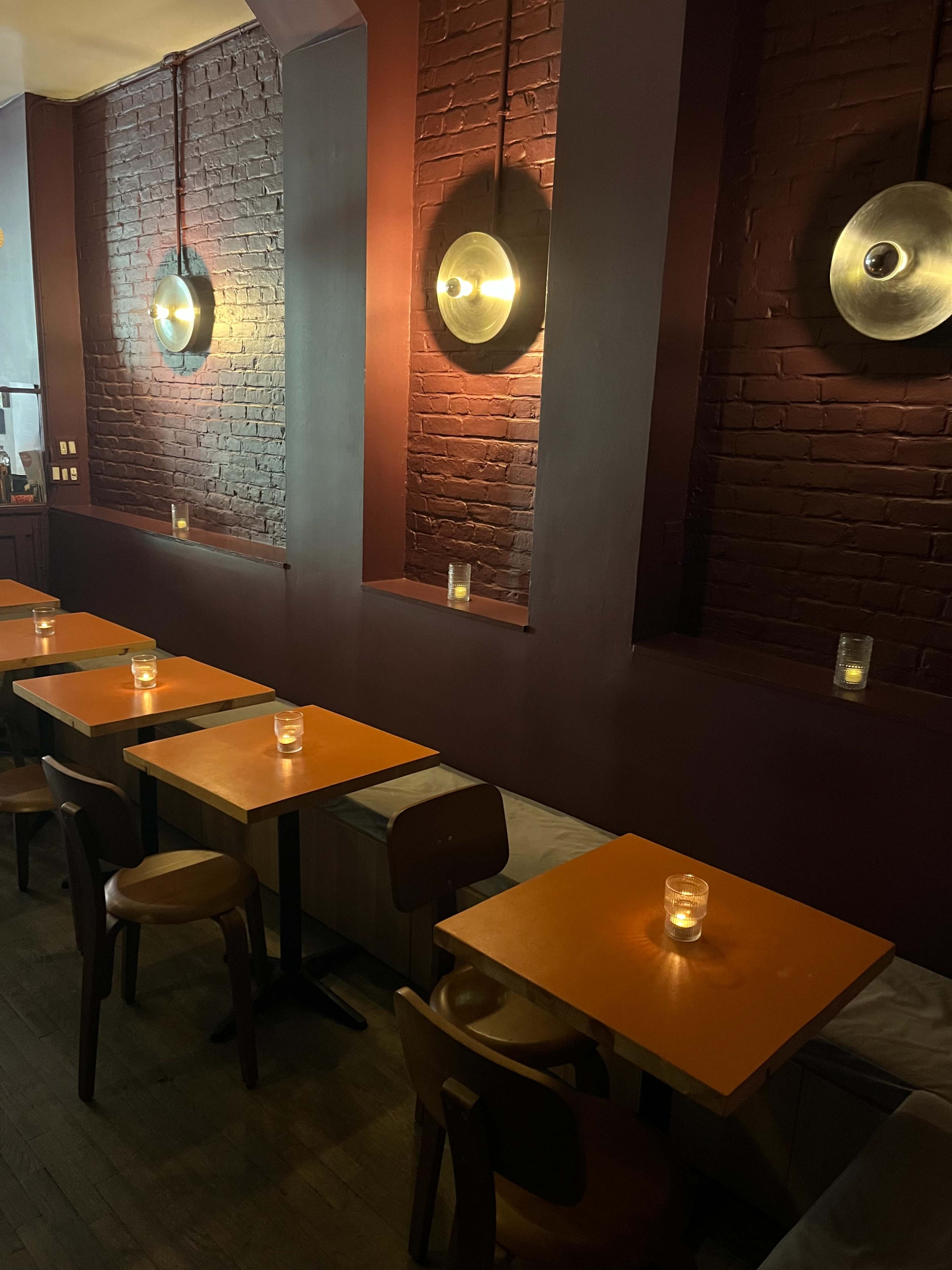 The image shows a dimly lit restaurant interior with wooden tables and chairs, illuminated by wall-mounted lamps and candlelight.