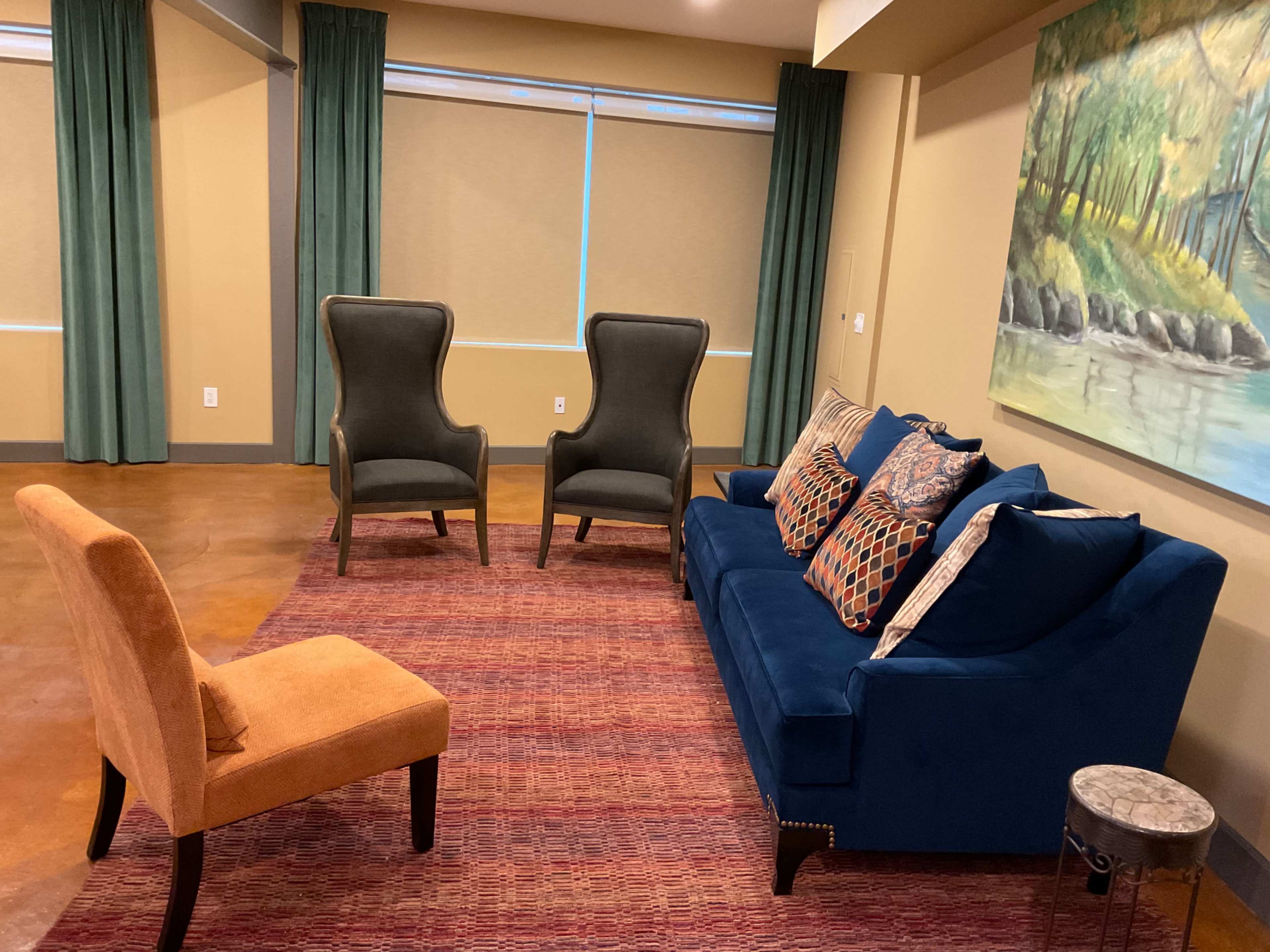 A living room with a blue sofa, two gray armchairs, a single orange chair, and a small side table placed on a textured rug.