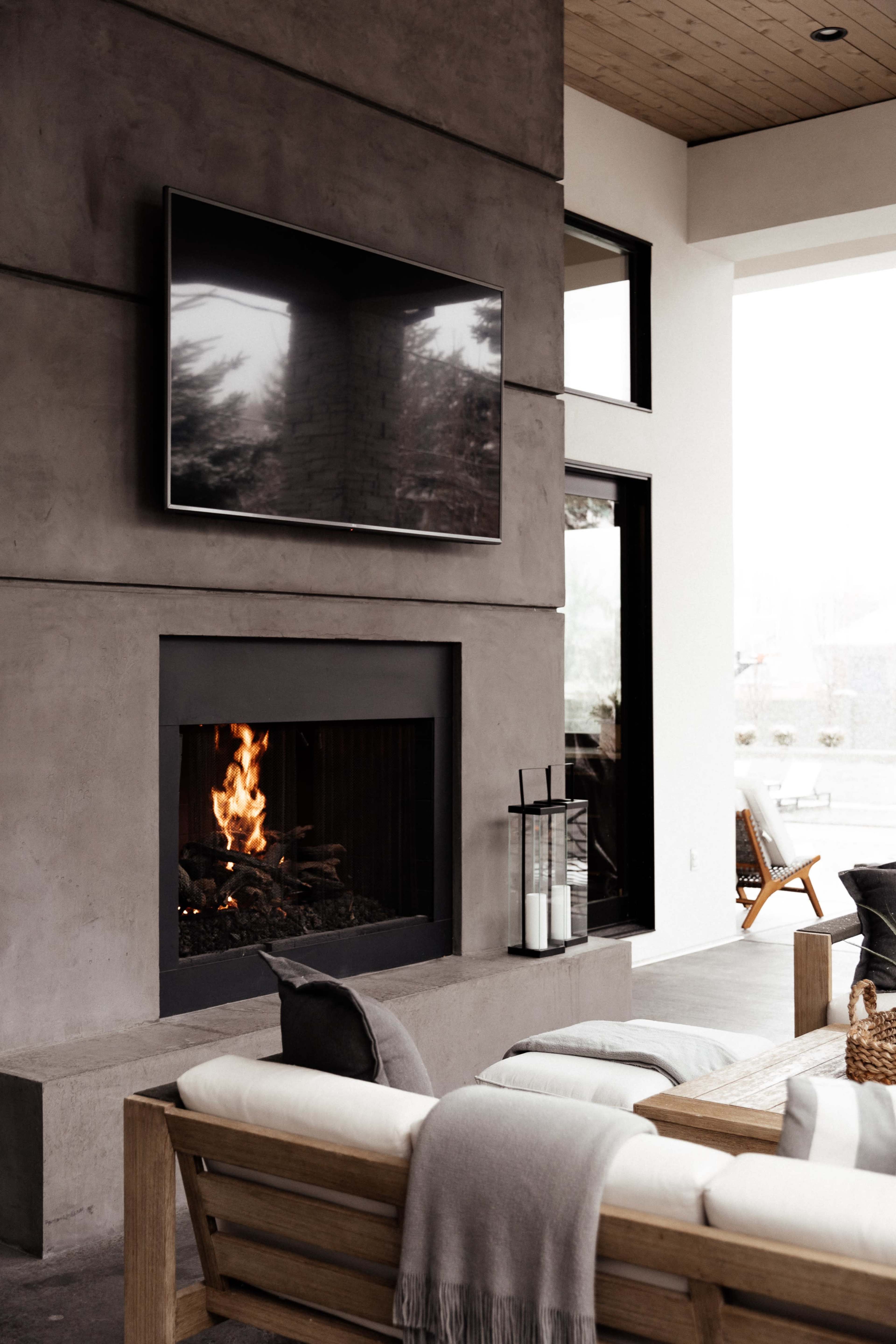 A modern living space with a concrete wall featuring a television above a fireplace, complemented by a wooden sofa with cushions and a coffee table.