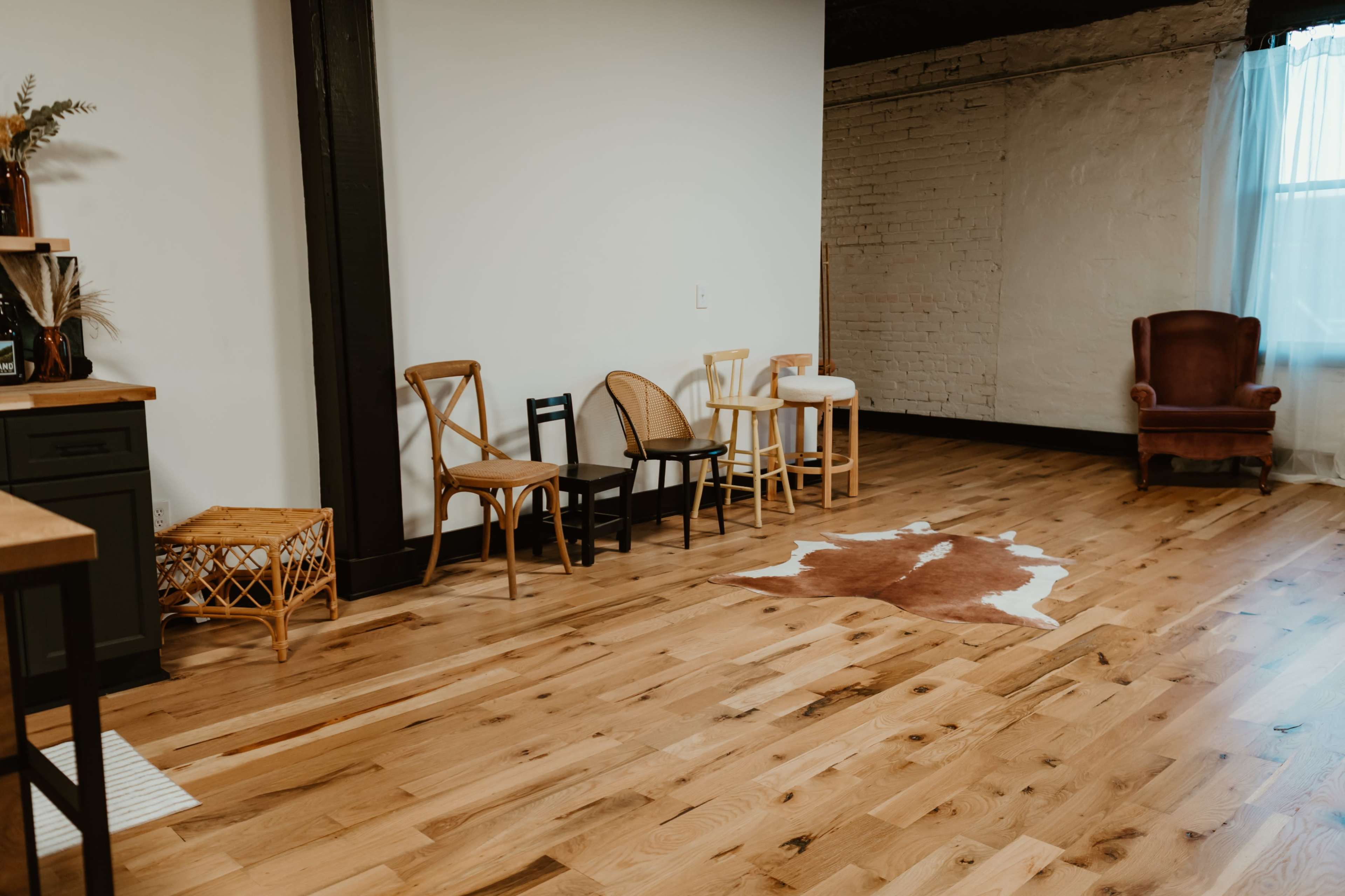 The room features a wooden floor with a variety of chairs arranged around a cowhide rug near a bare wall.