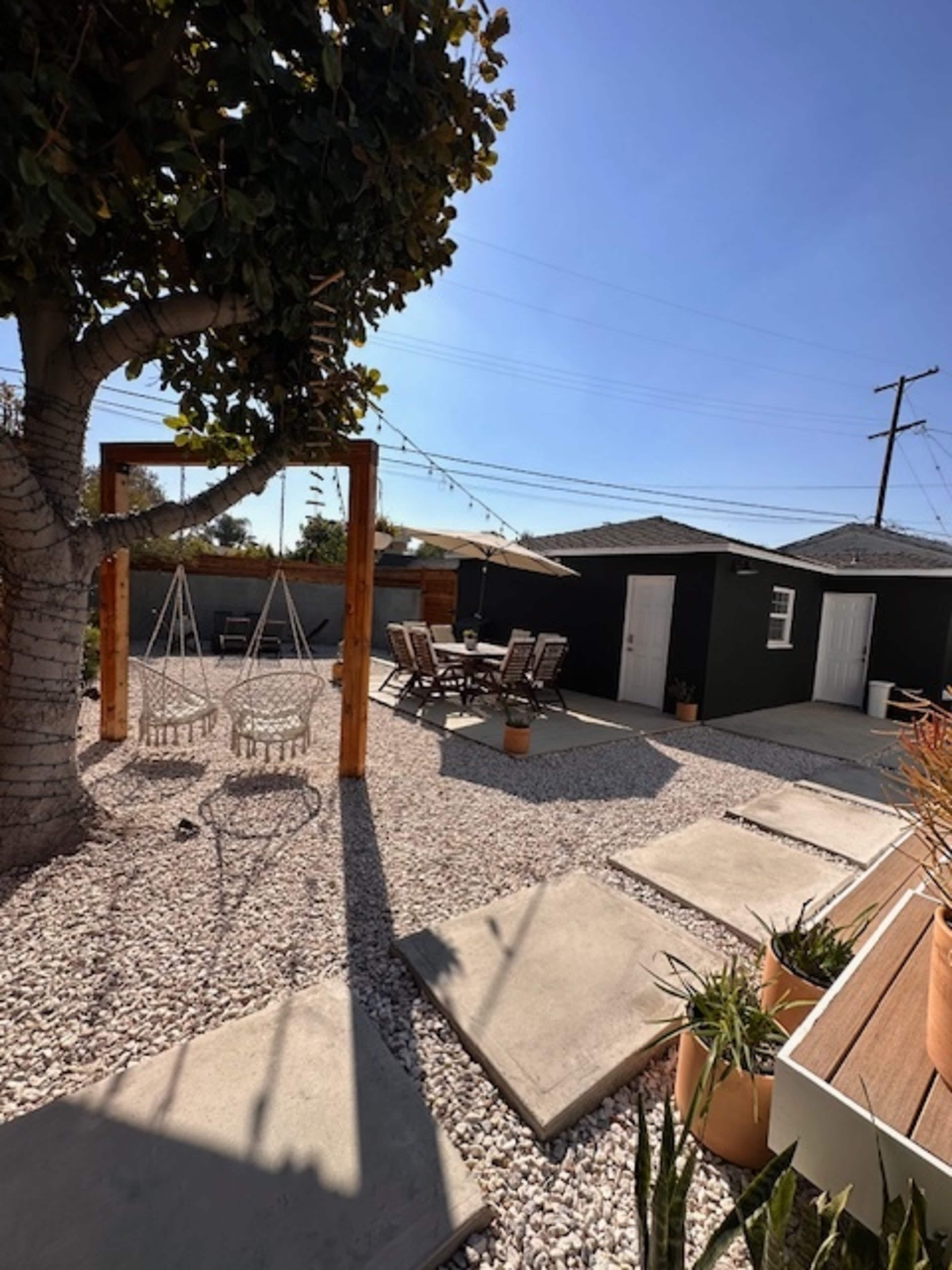 A courtyard with two hanging chairs, a seating area with wooden chairs, and a gravel landscape surrounded by buildings.