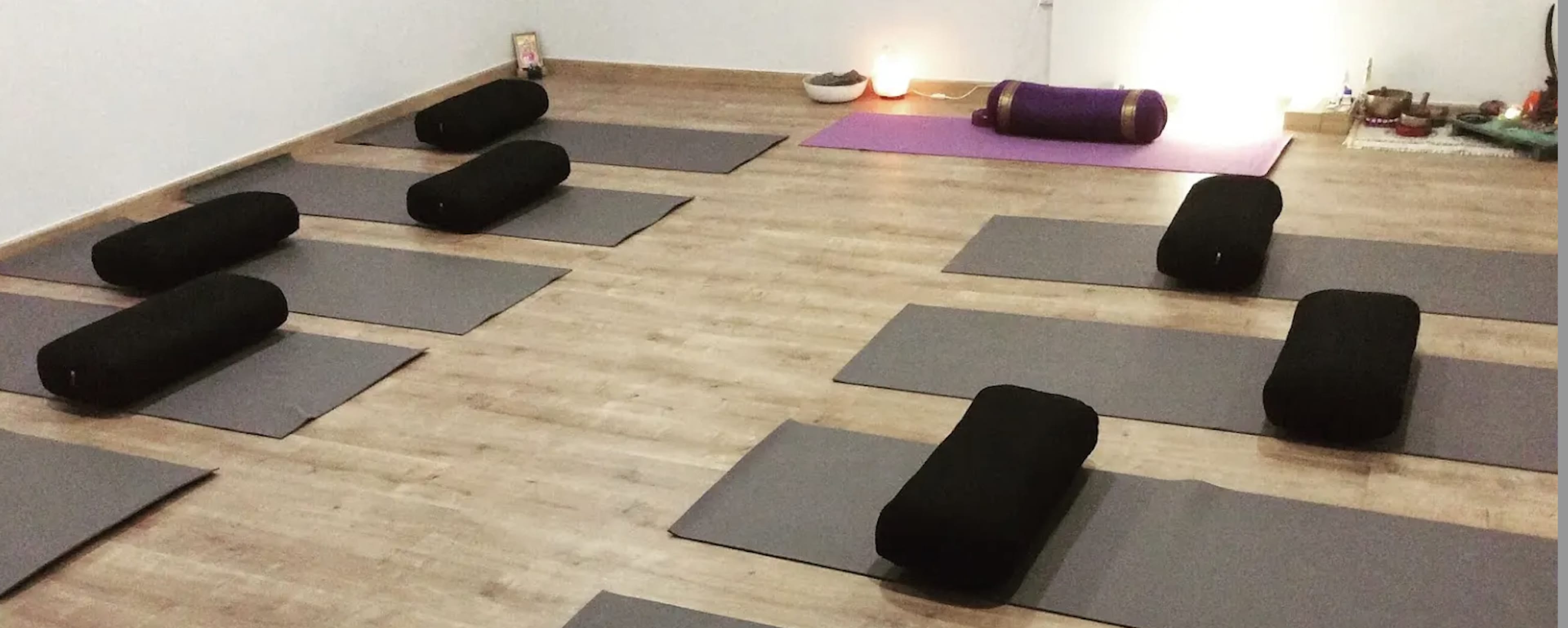 A yoga studio with black bolsters placed on gray mats arranged neatly across a wooden floor, with a purple mat set up at the back.