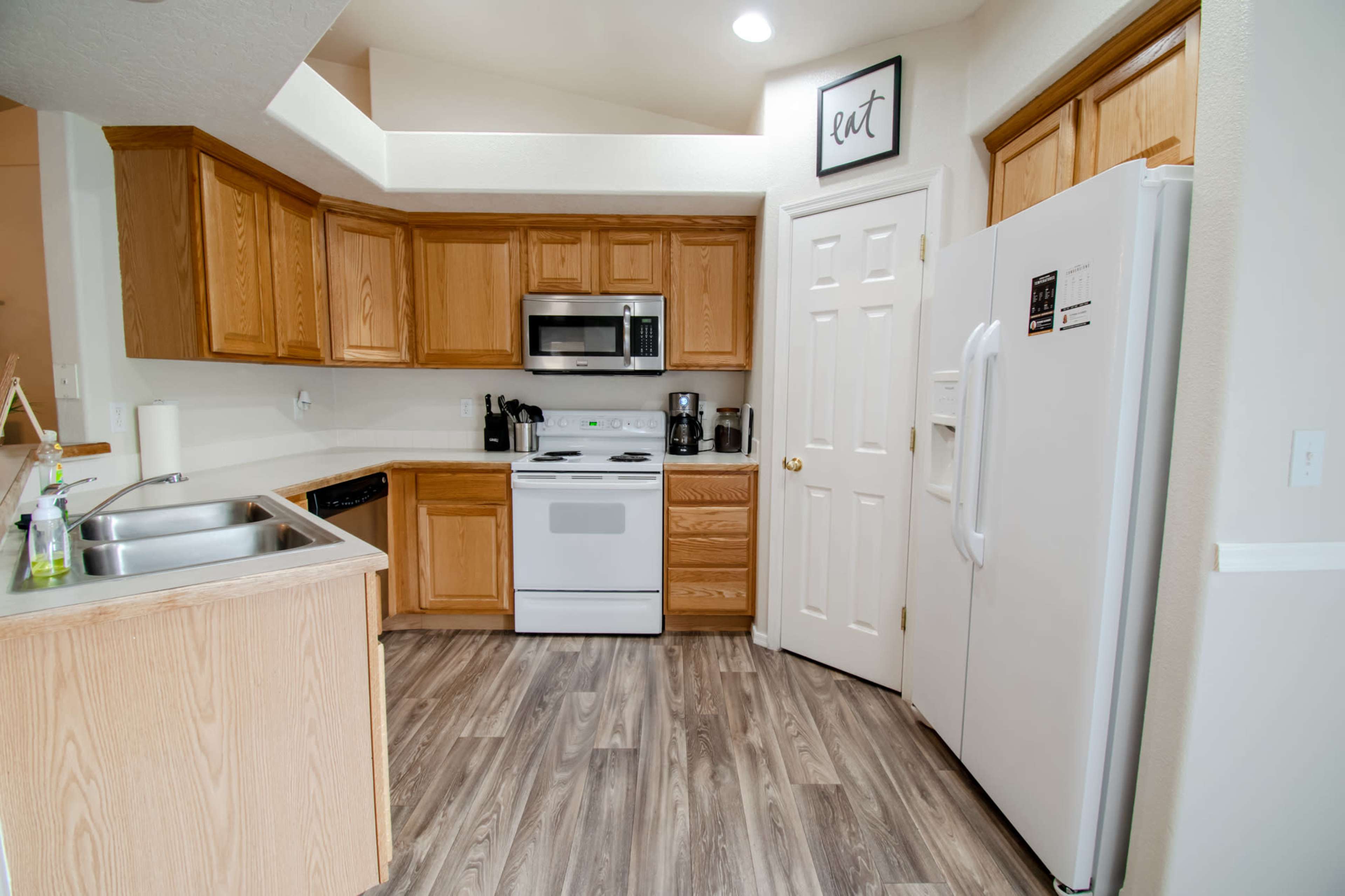 A compact kitchen with wooden cabinets, white appliances, and a light-colored countertop.
