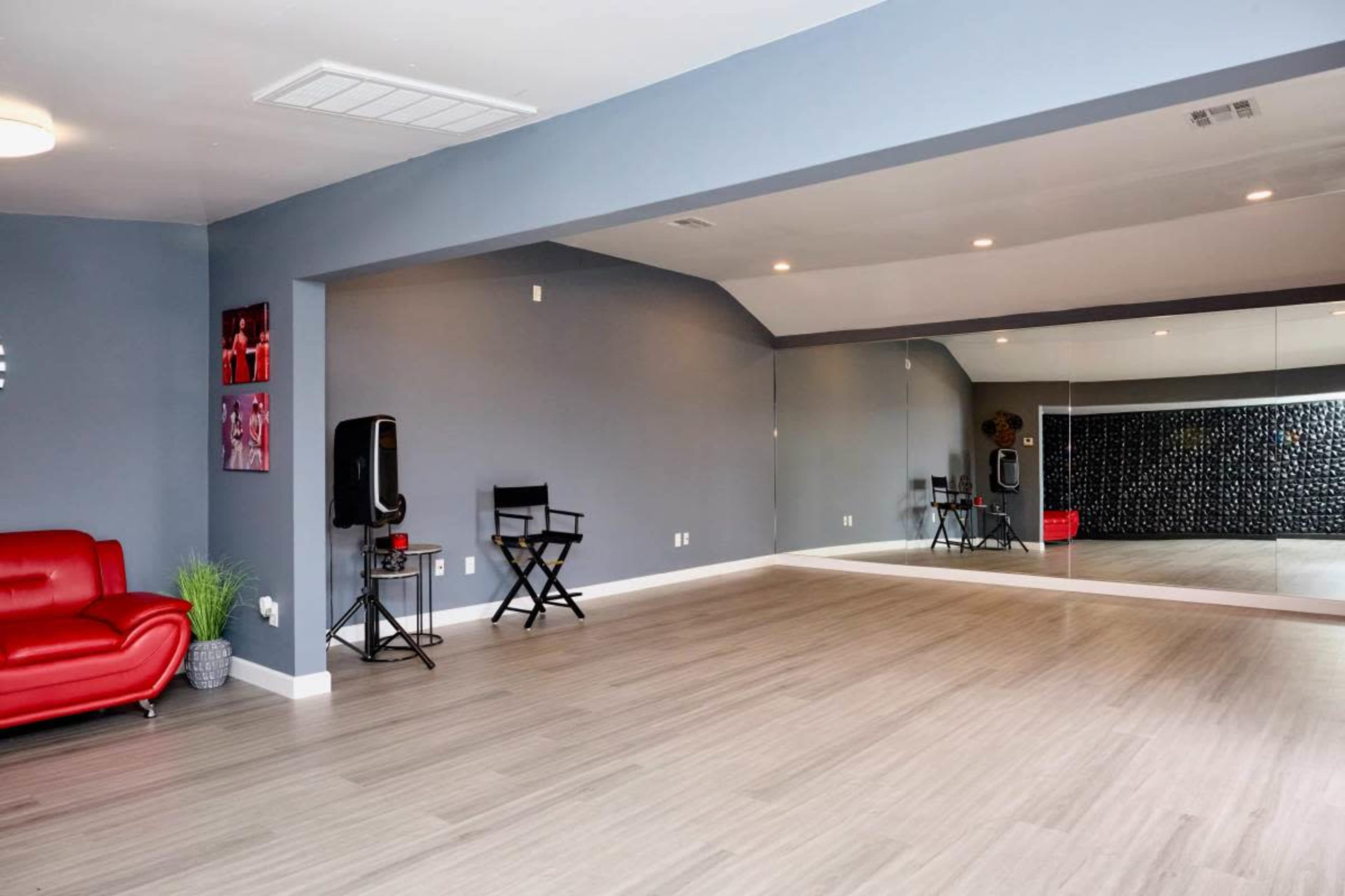 The image shows a spacious dance studio with a large mirrored wall, a red sofa, and a director's chair in one corner.