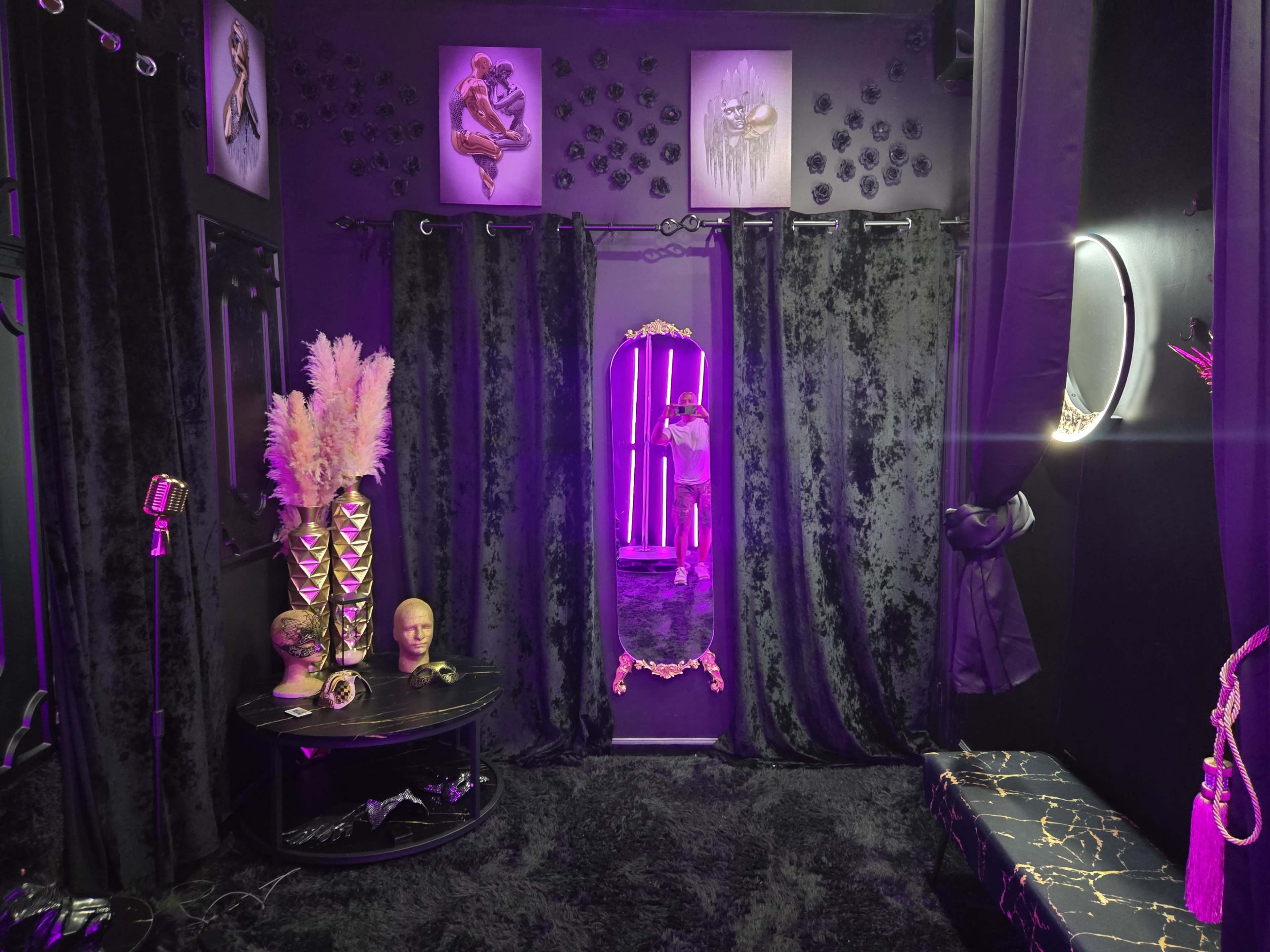 The image shows a dark, elegantly decorated room with black curtains, a large mirror framed in gold, and purple lighting creating a moody atmosphere.