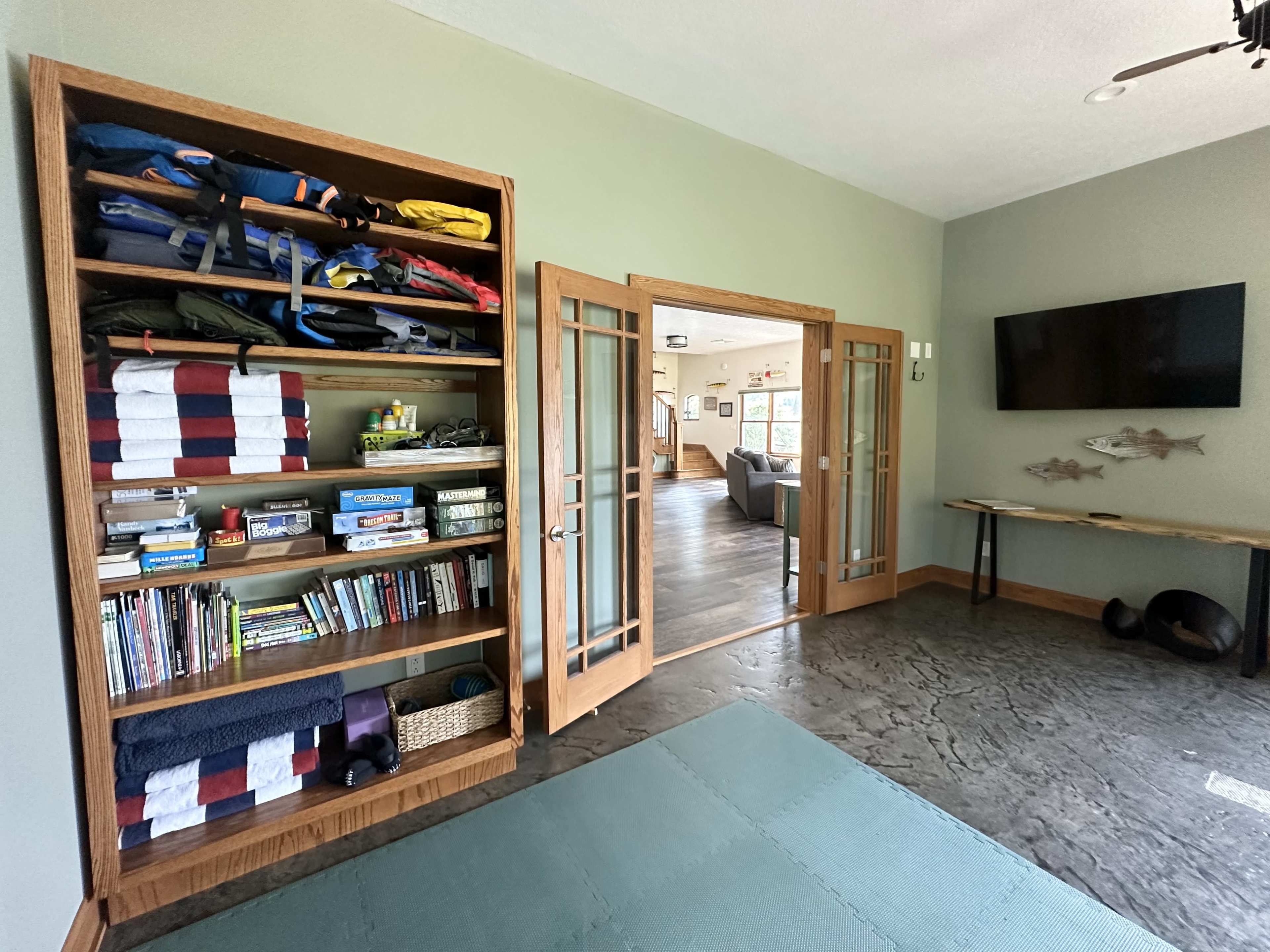 A room with a wooden shelf filled with various items, an open door leading to another area, and a wall-mounted television.
