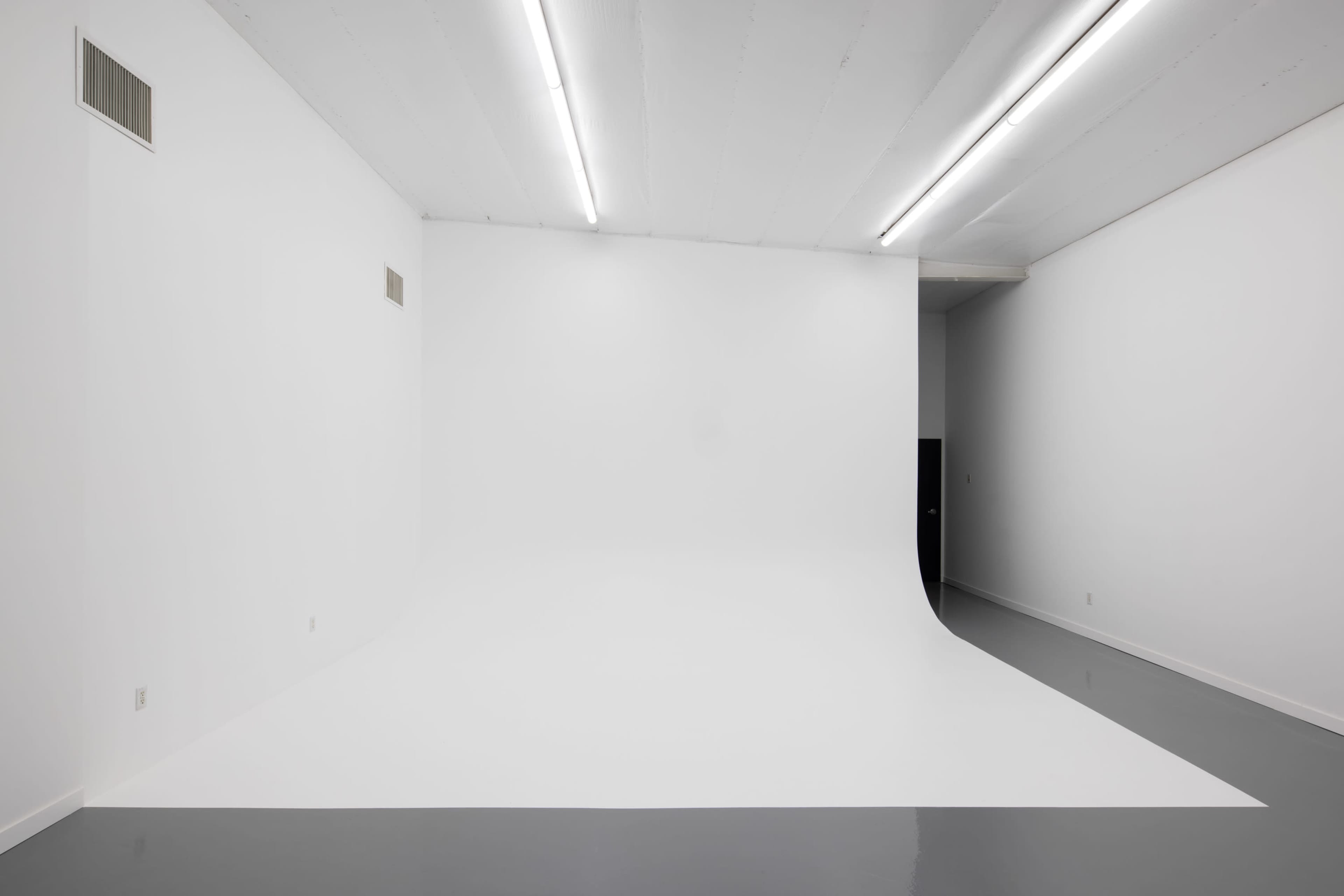 A spacious, empty studio with a seamless white backdrop and a shiny gray floor.