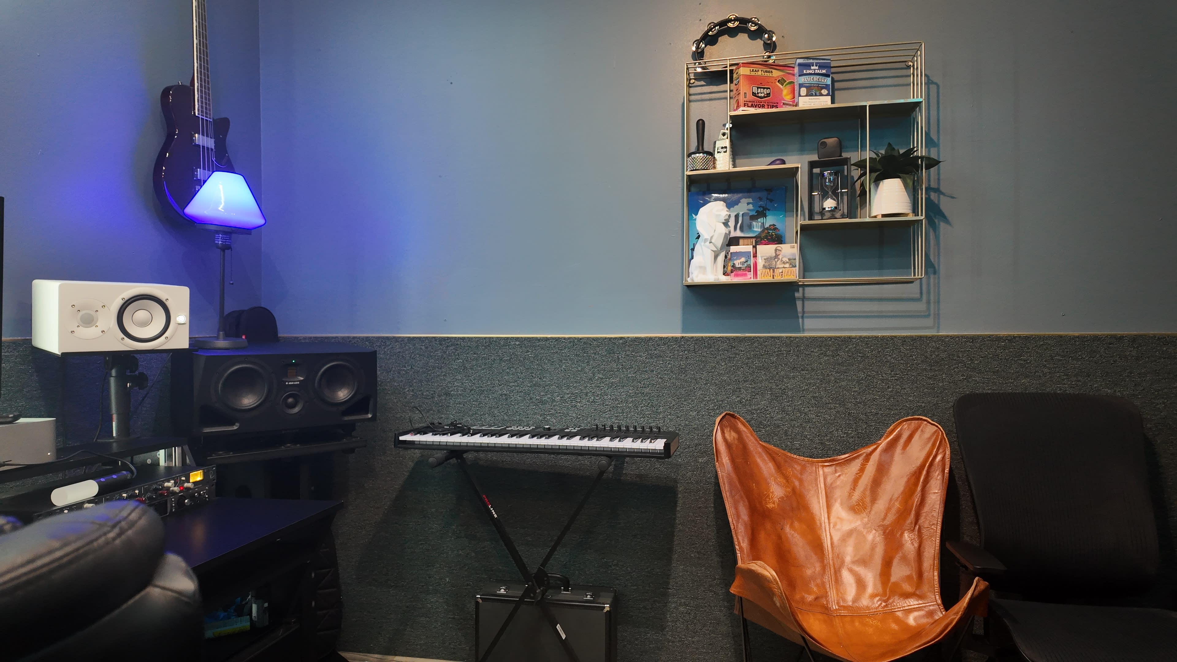 The image shows a home studio corner featuring a keyboard, audio equipment, a shelf with decorative items, and a chair.