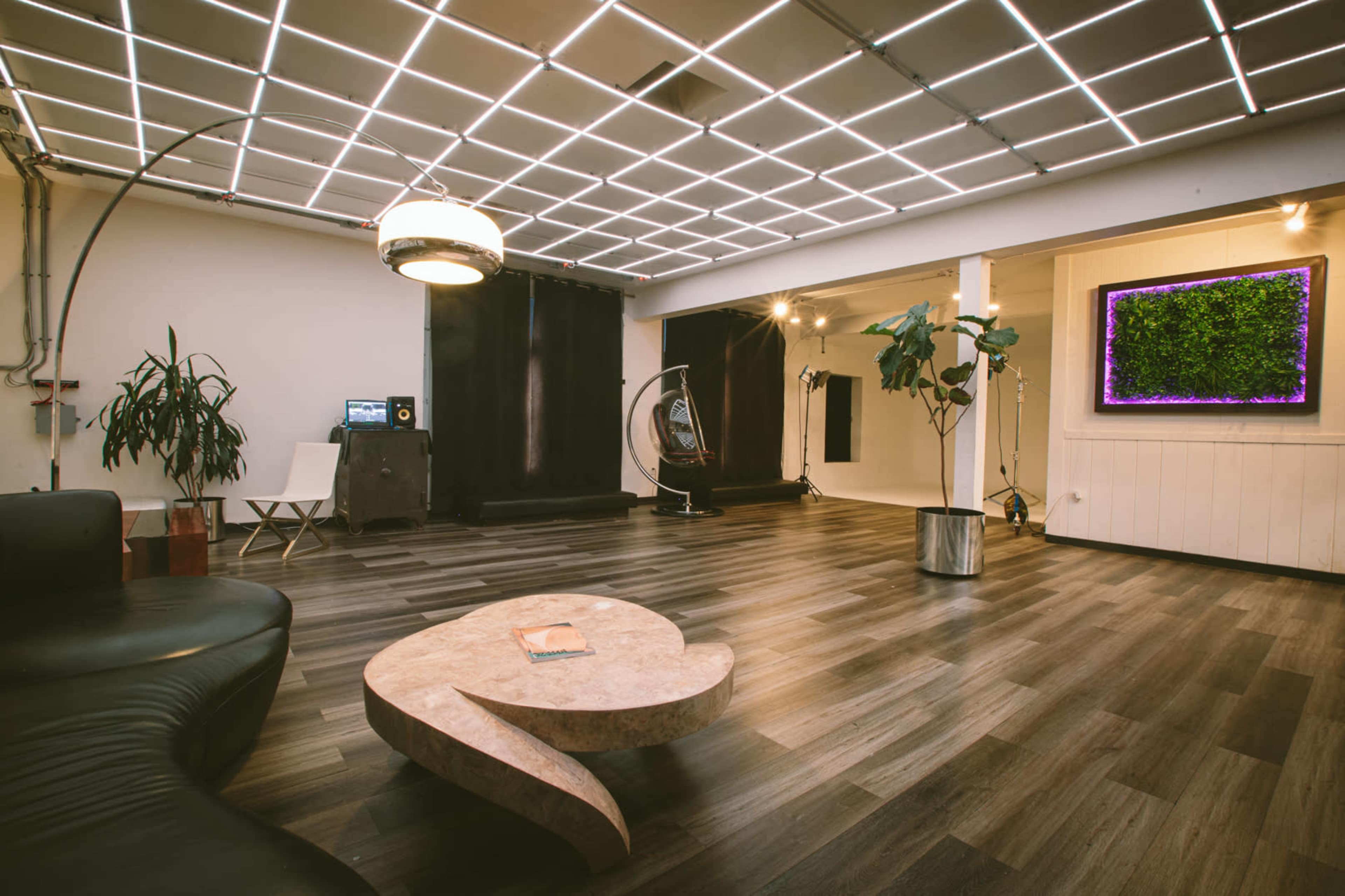 A spacious room with a modern design, featuring a curved marble coffee table, a black couch, and a wall-mounted screen displaying greenery.