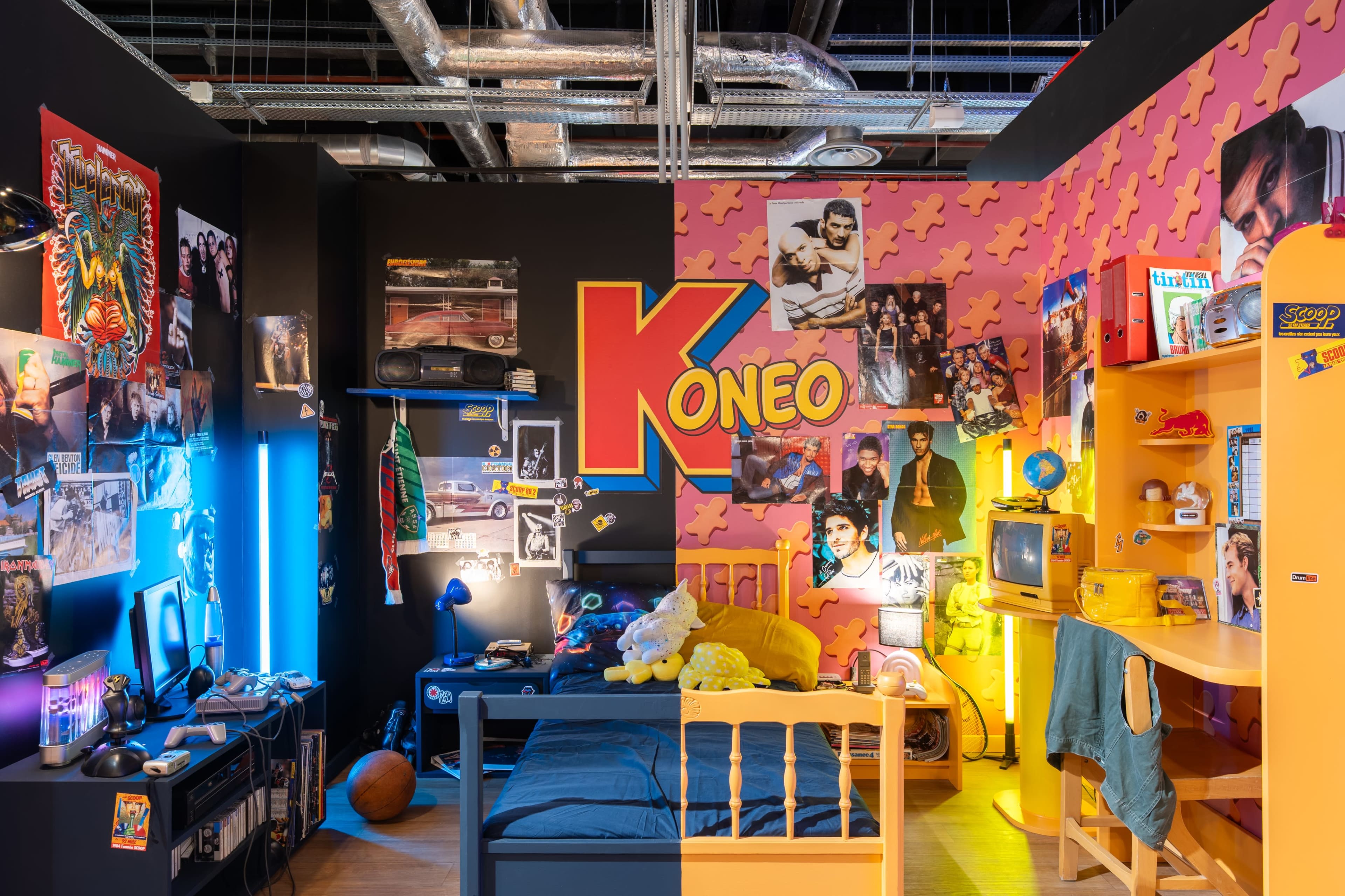 The image shows a split room with one side decorated in dark colors and rock memorabilia, while the other side features bright colors and pop culture themes, including a workspace with a yellow desk and retro TV.