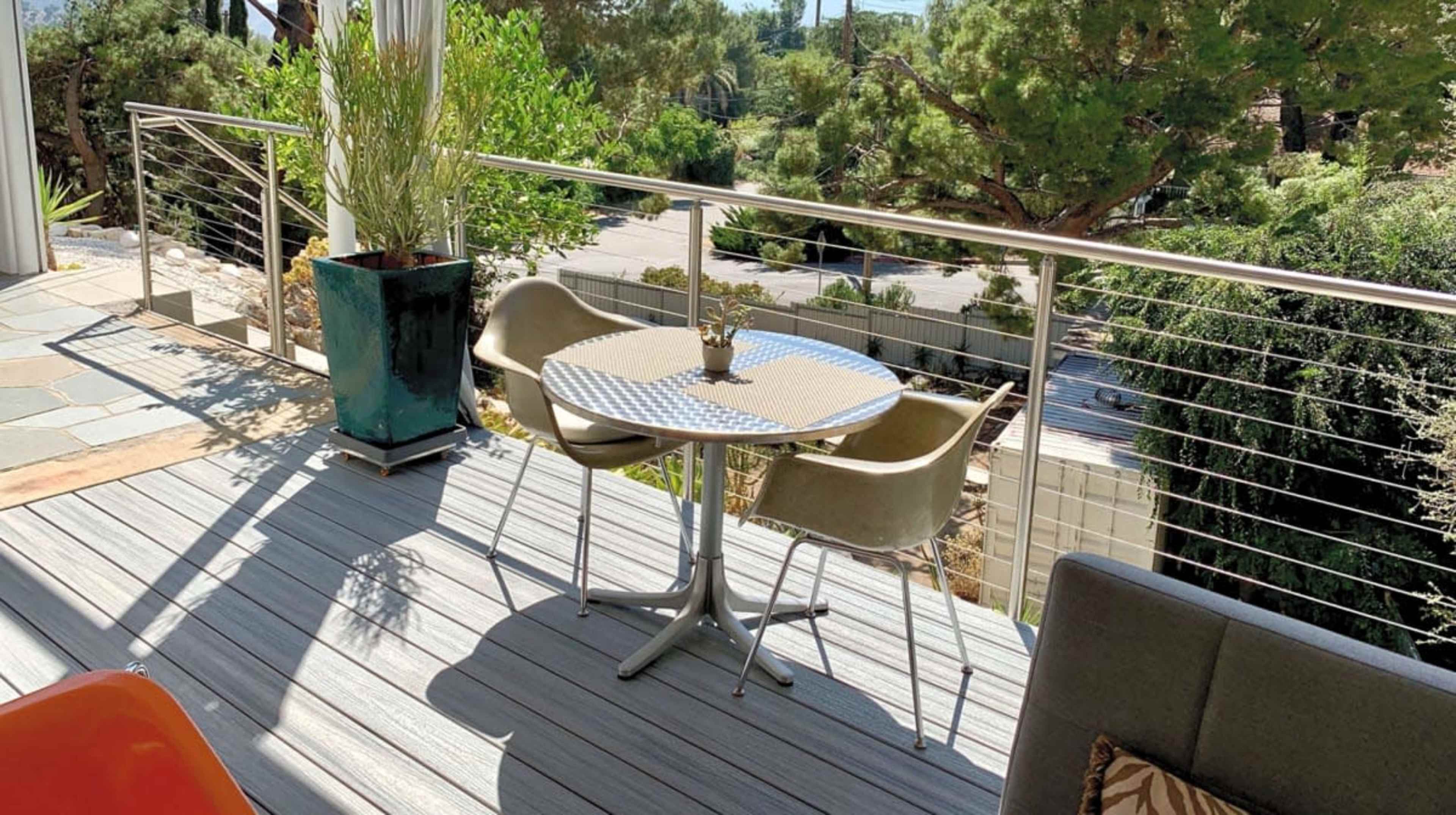 A small table with two chairs is set up on a patio surrounded by greenery and a railing.