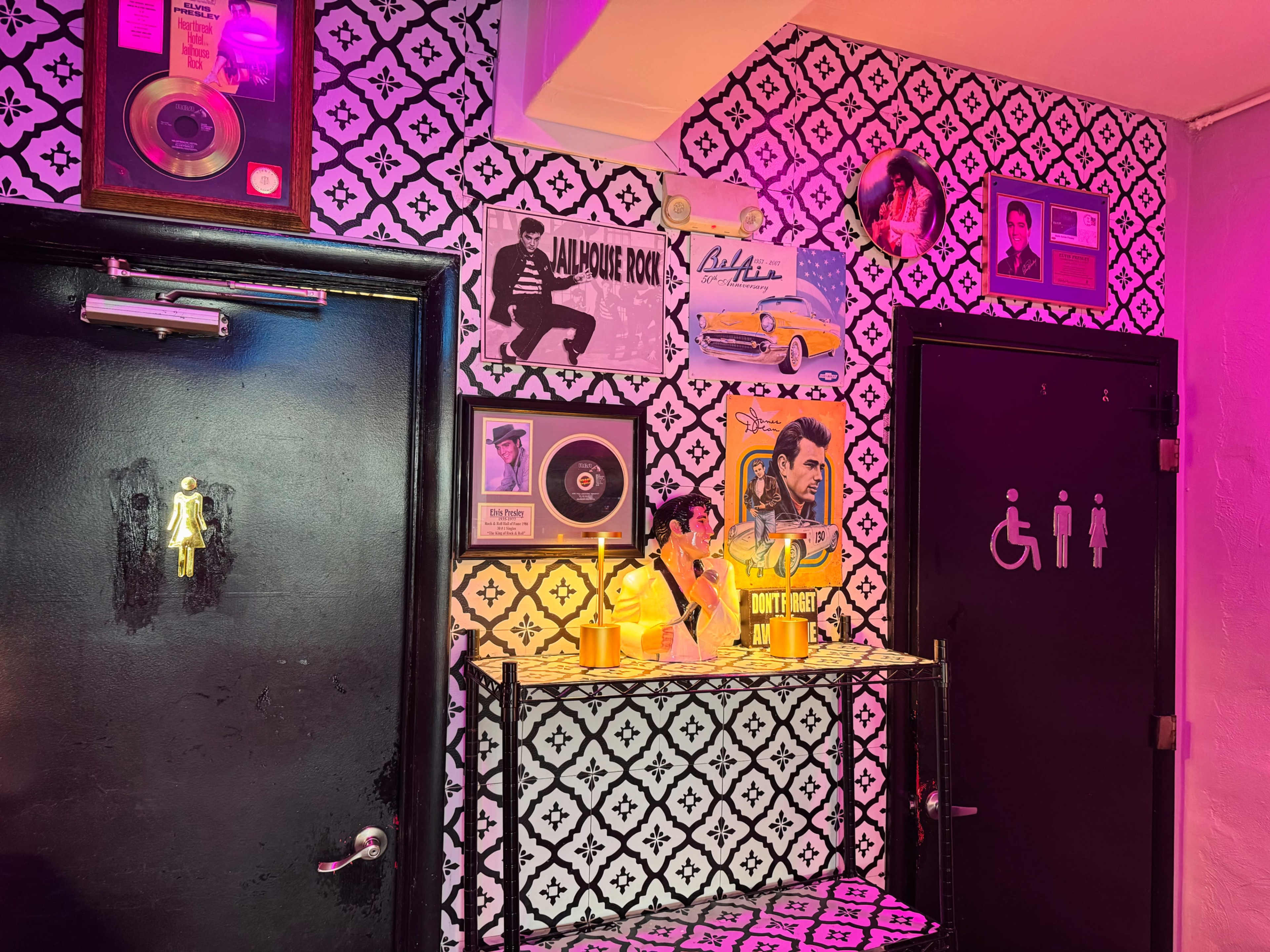 The image shows a brightly colored wall adorned with vintage music posters, a record, and a shelf displaying decorative items near a door with a bathroom sign.