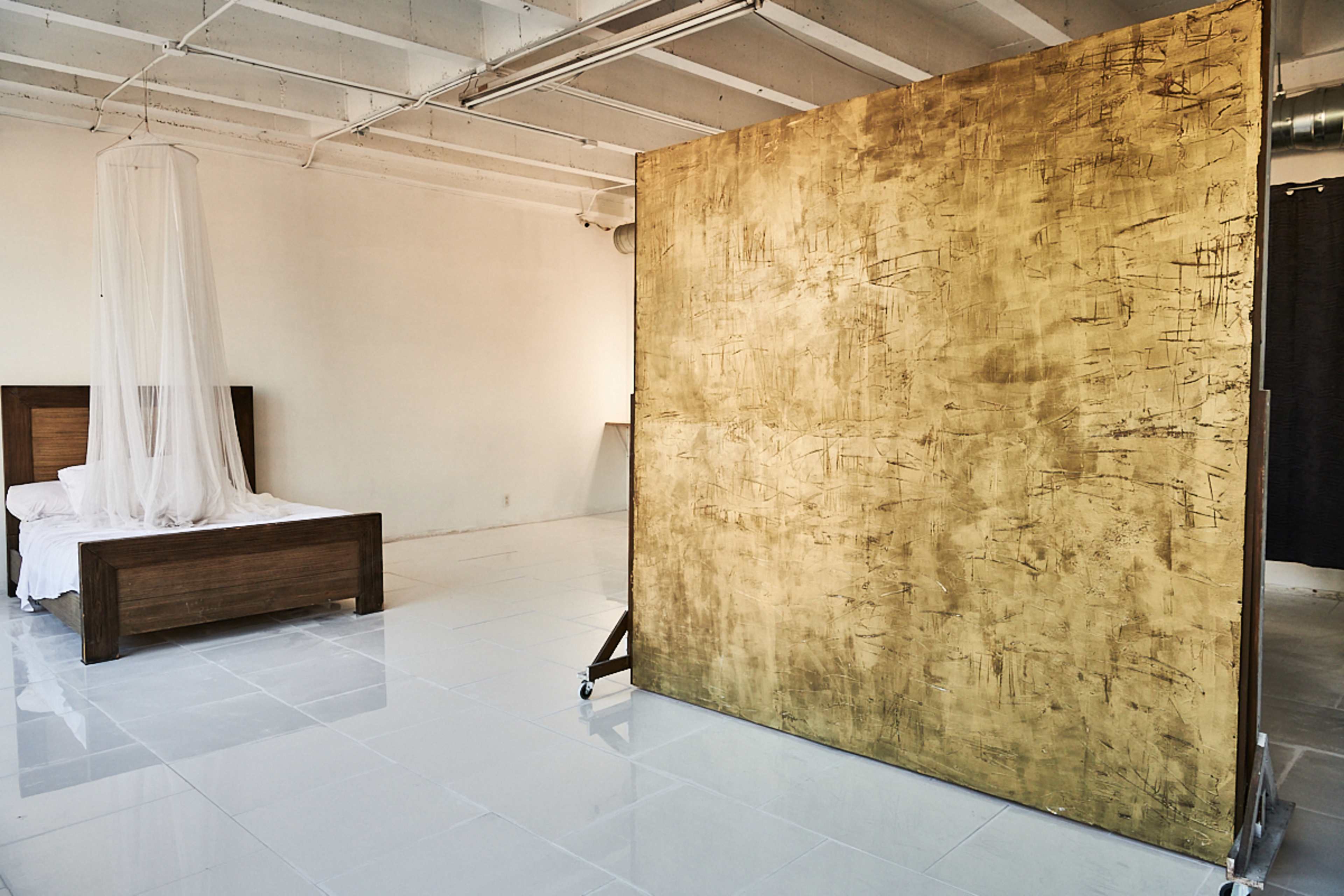 A spacious room features a wooden bed with a canopy and a large gold-painted partition.