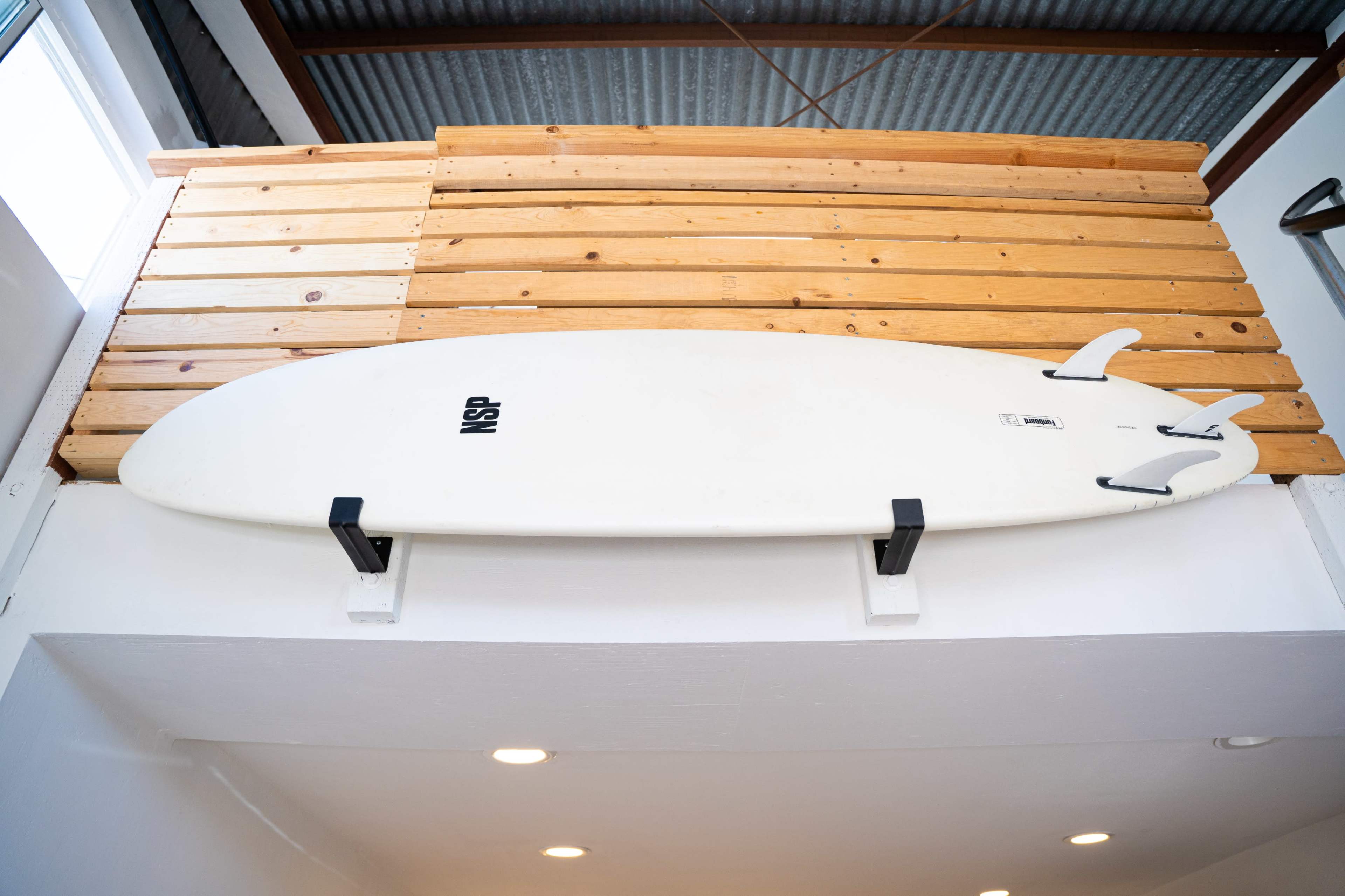 A surfboard is mounted on a wooden wall, positioned above a white section of the room.