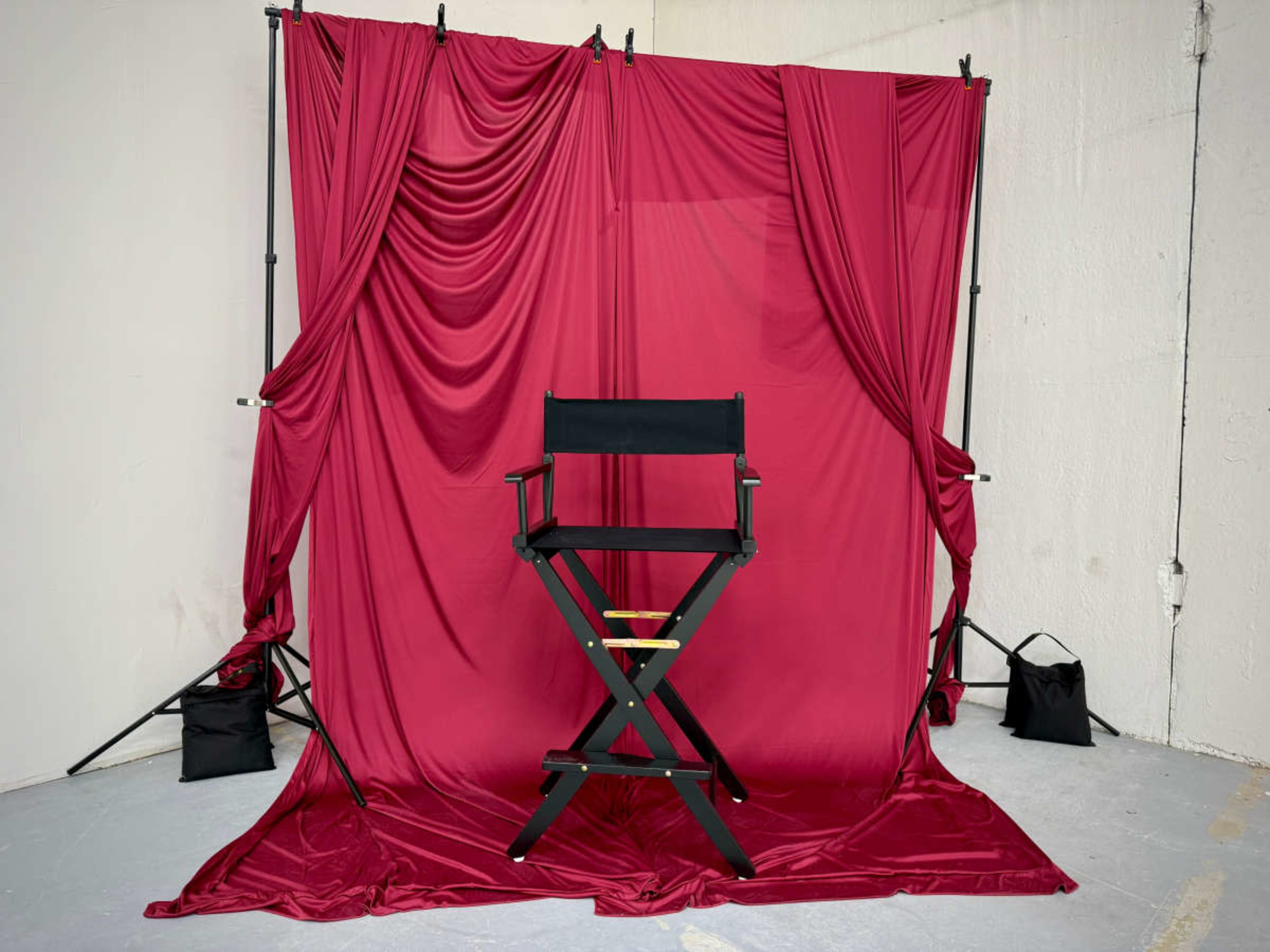 A black director's chair is positioned in front of a red draped backdrop in an indoor setting.