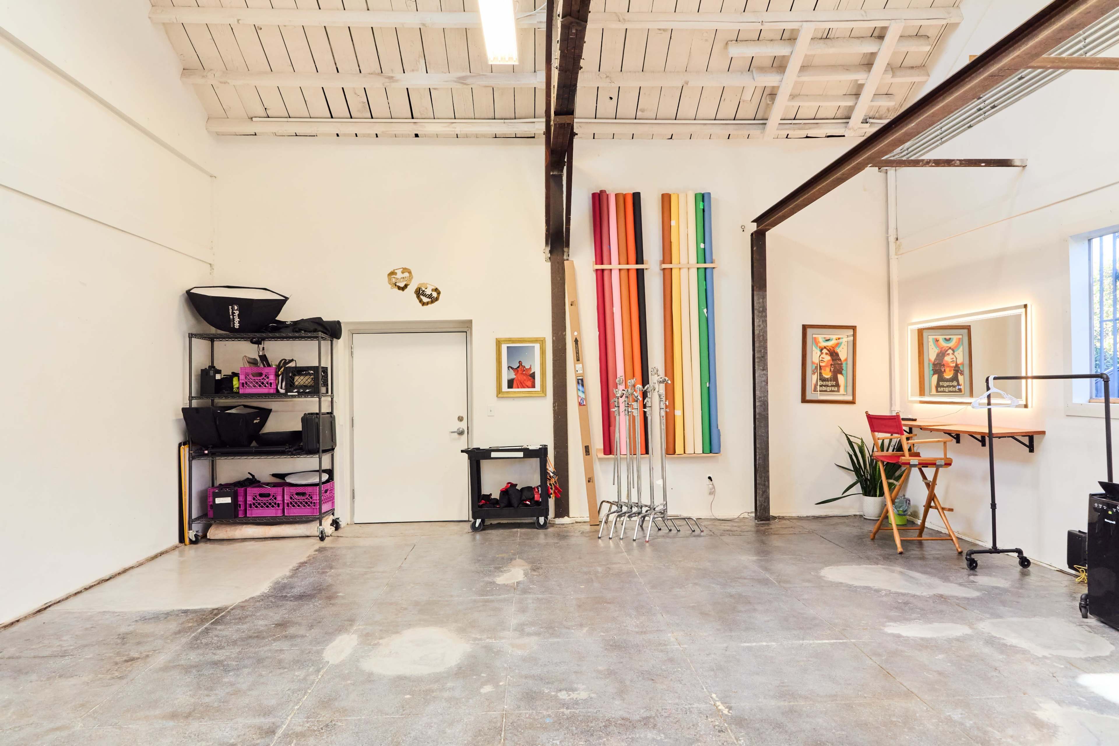 The image shows a spacious, well-lit studio with exposed beams, colorful vertical panels, and a variety of equipment organized along the walls.