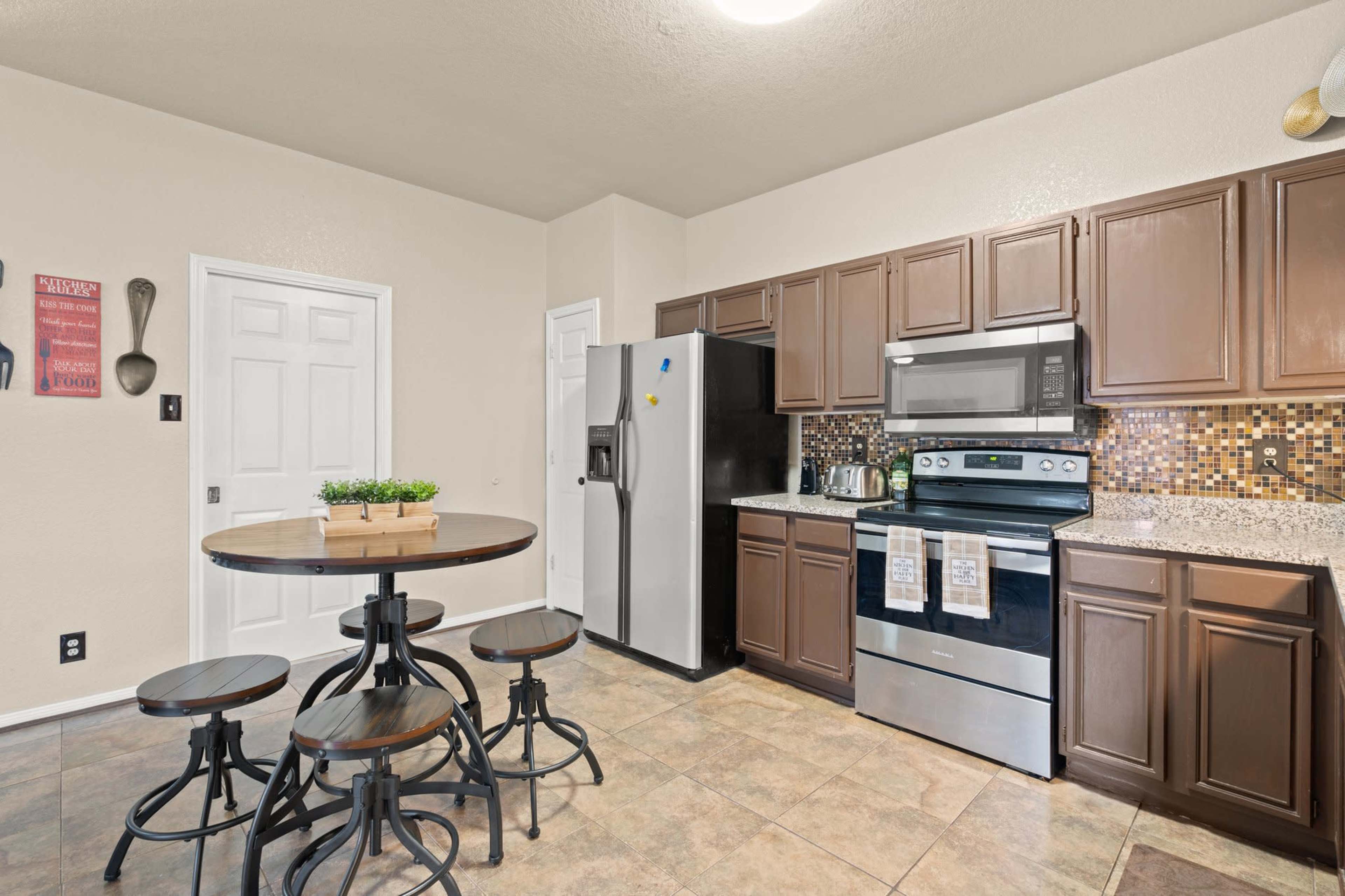 A modern kitchen featuring dark wooden cabinets, stainless steel appliances, and a round dining table with four chairs.