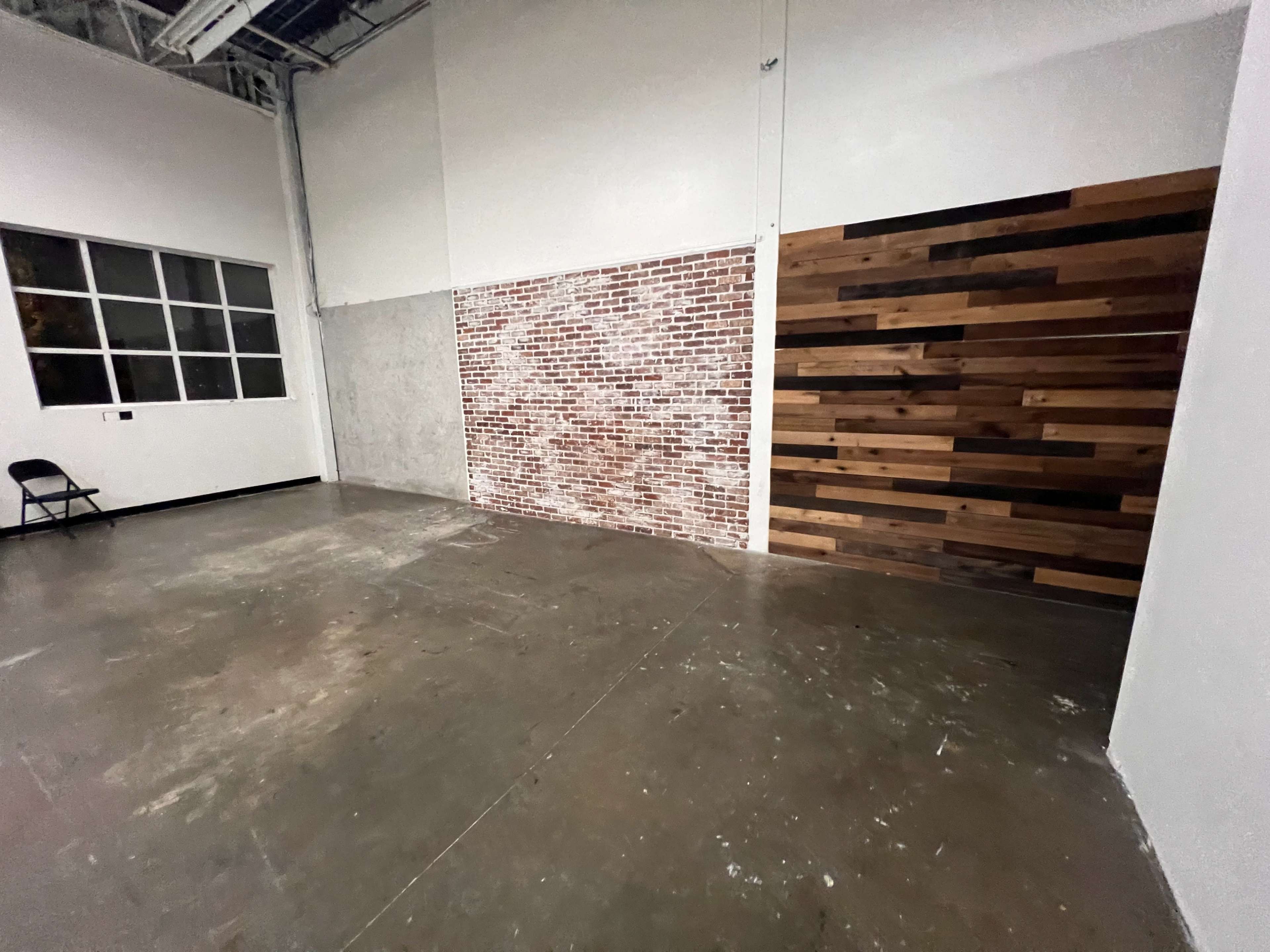 An empty room with a concrete floor, a brick wall, and a wooden accent wall.