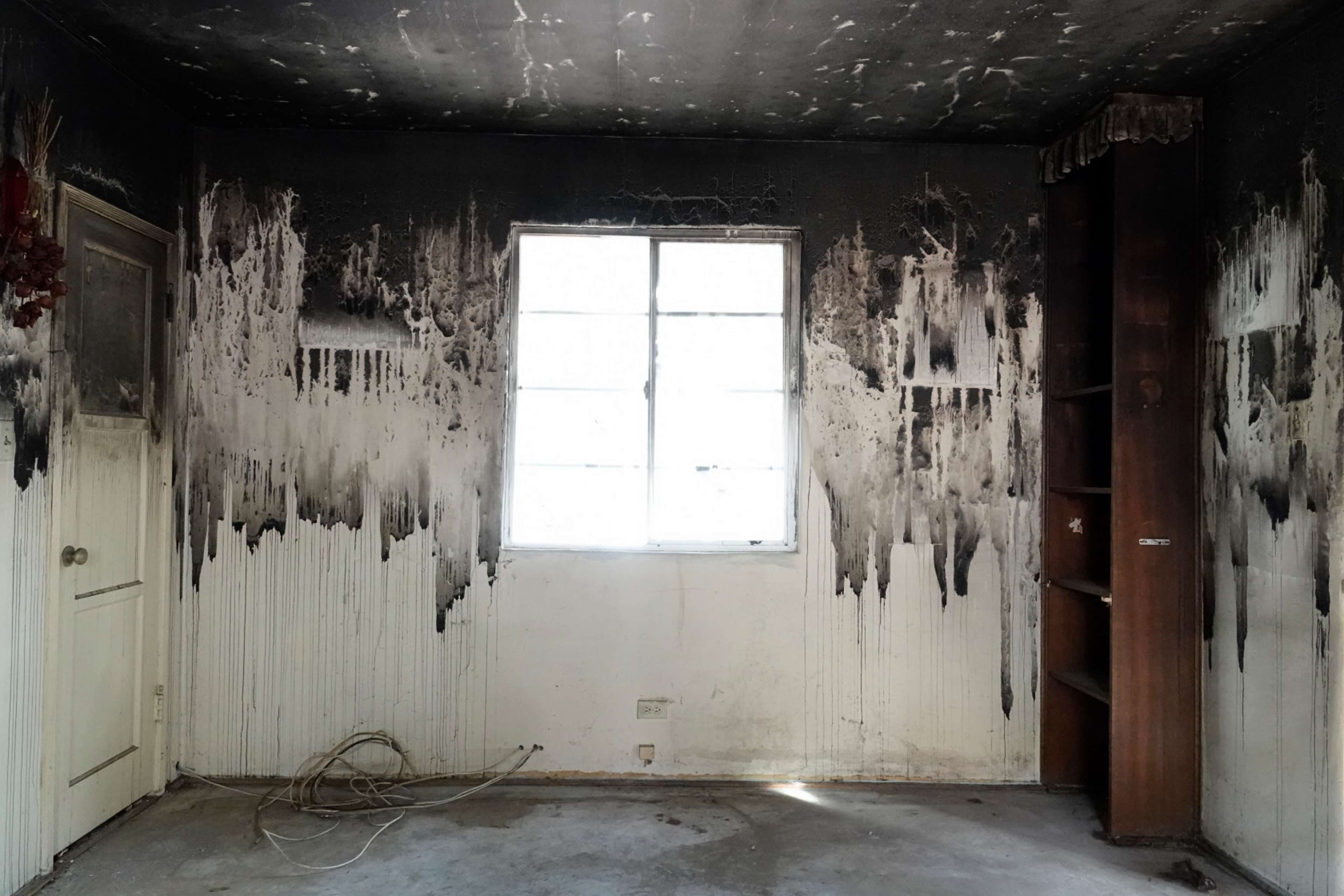 The room features charred walls with streaks of black soot and a window allowing light to filter into the space.