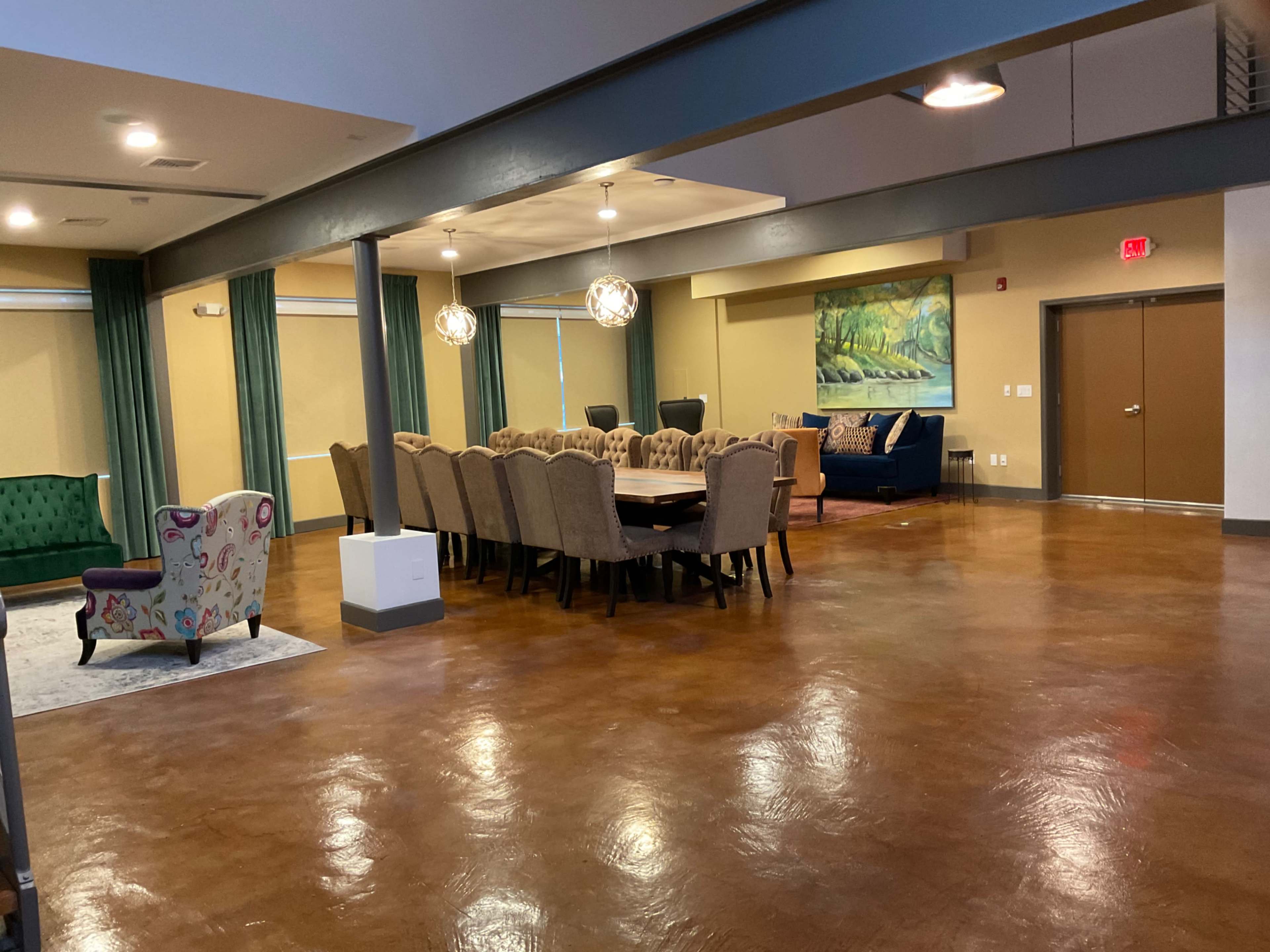A spacious room with a large dining table surrounded by chairs, a seating area with a green sofa, and decorative lighting fixtures.