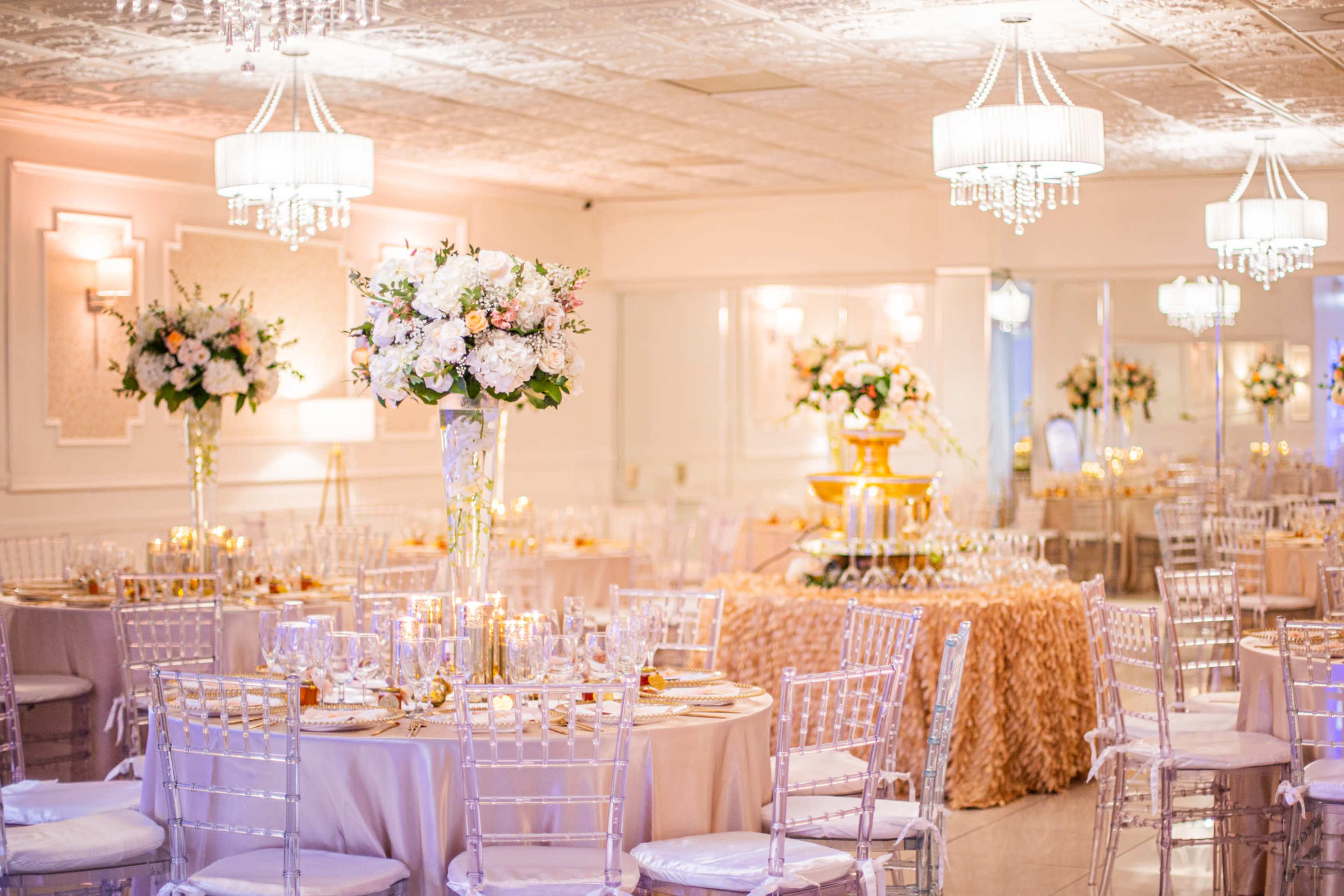 The image shows a elegantly decorated event space with tables set for a formal banquet and floral arrangements on stands.