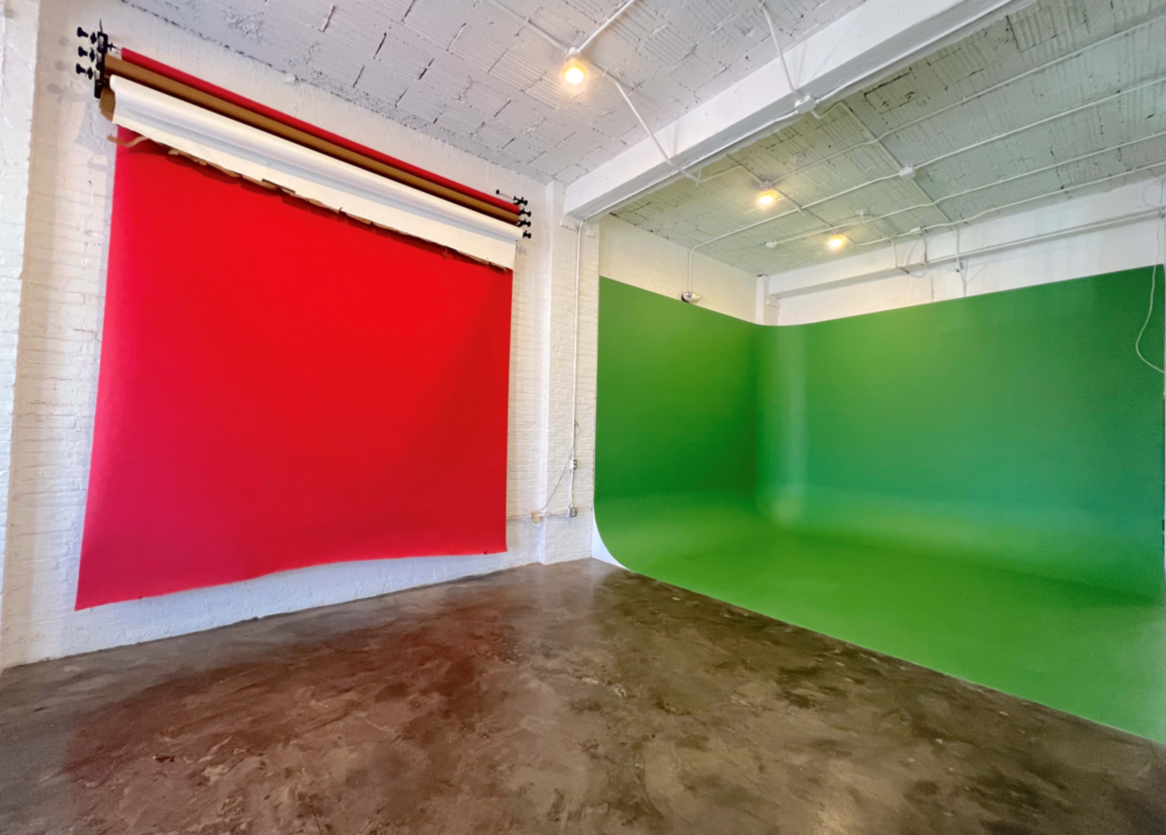 A studio space with a red backdrop on one side and a green backdrop on the other, against a polished concrete floor and white walls.