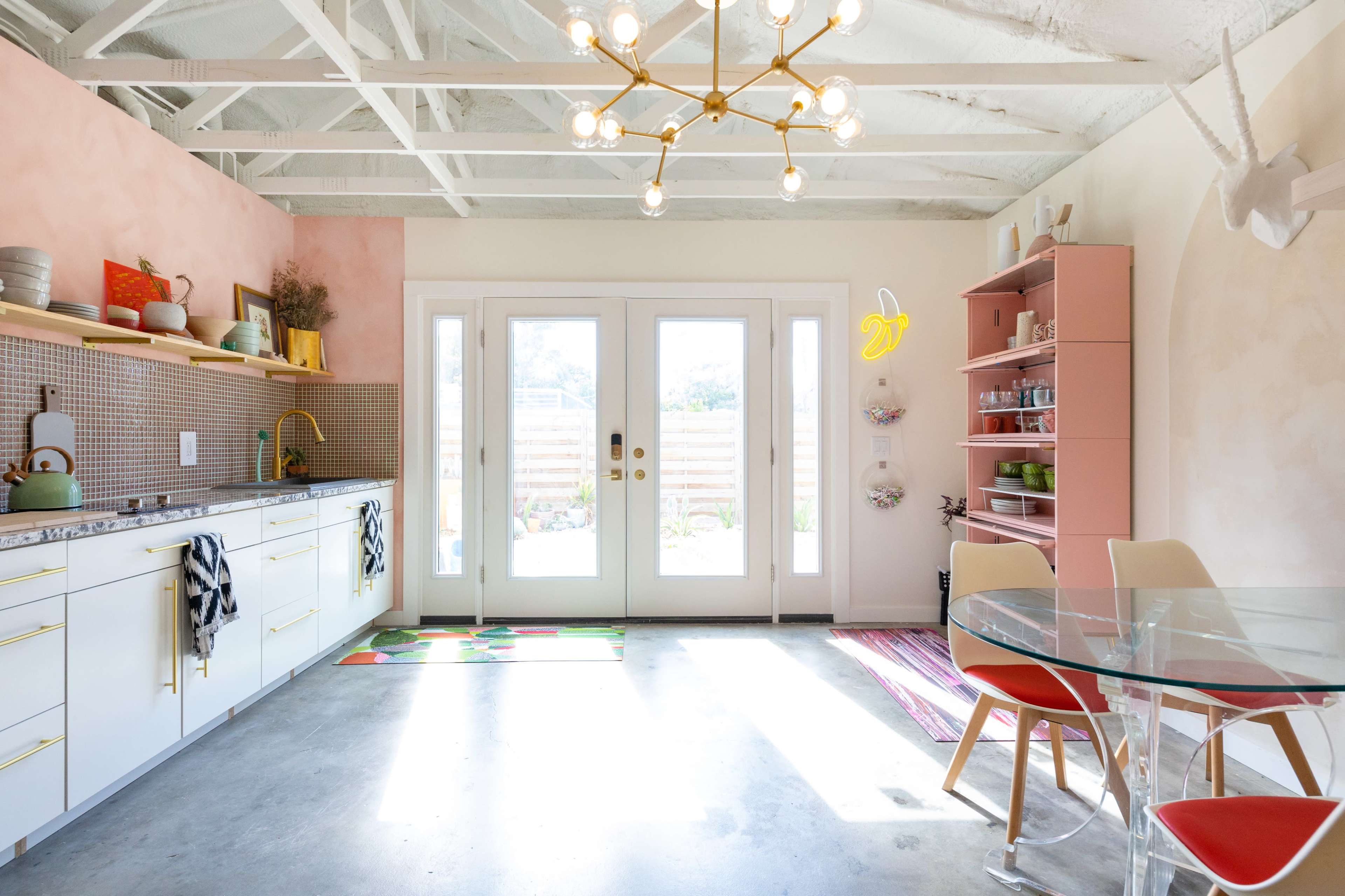 A modern kitchen features a light color scheme, a large window with double doors, and a combination of open shelving and cabinetry.