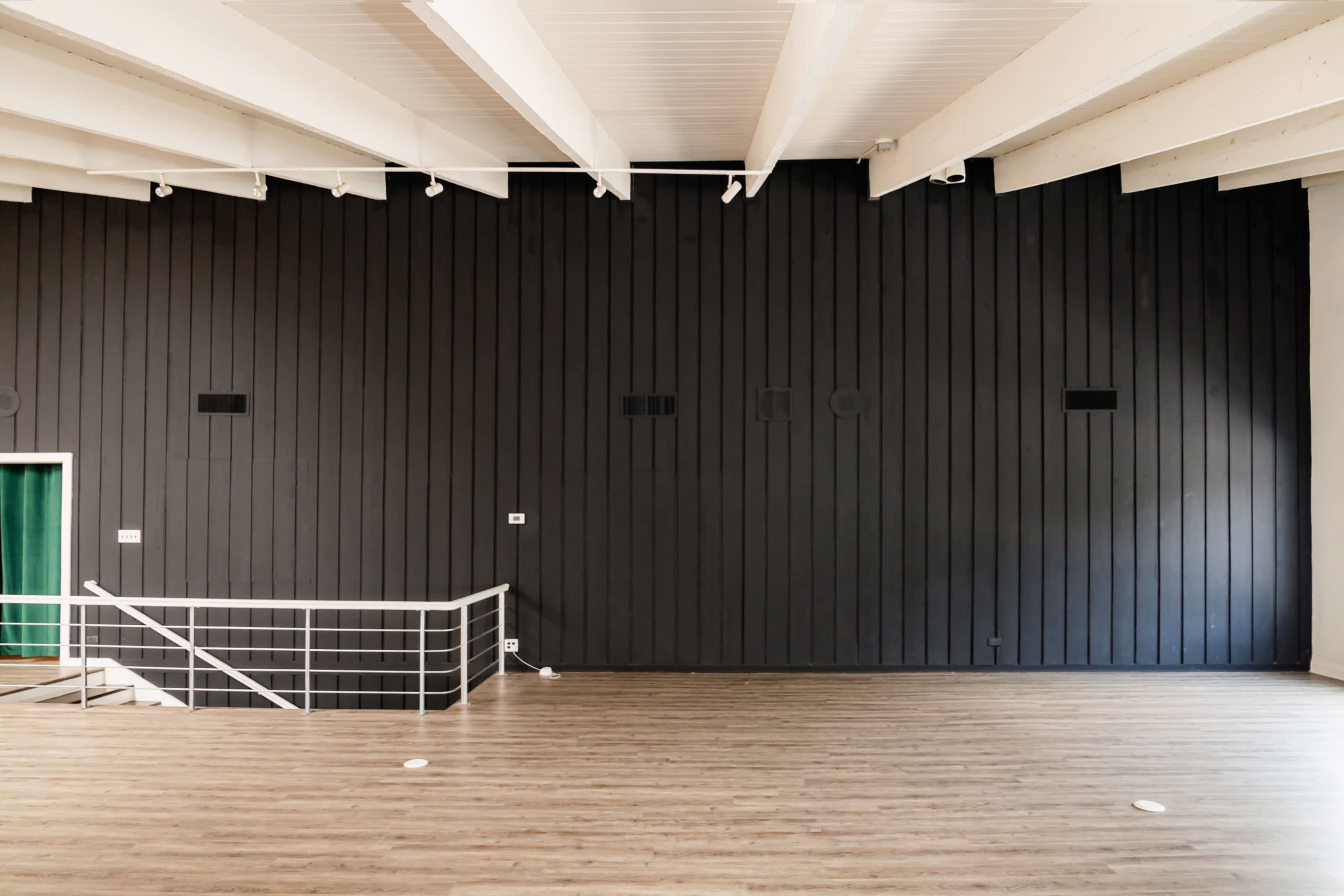 A spacious room with a dark wooden wall, a white railing, and wooden flooring.
