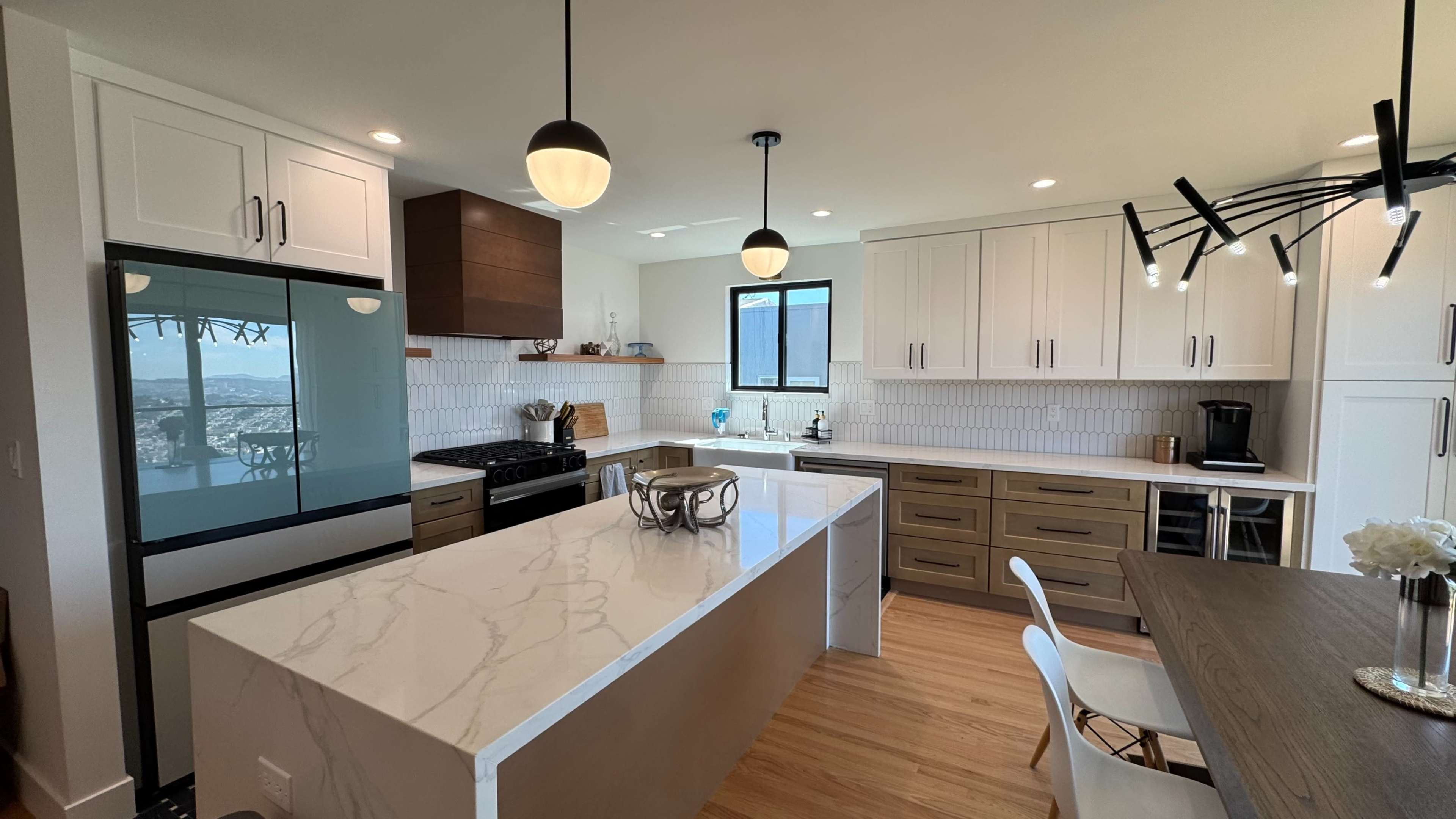 The image shows a modern kitchen featuring a large island with a white marble countertop, light wood cabinetry, and a combination of open and closed storage spaces.