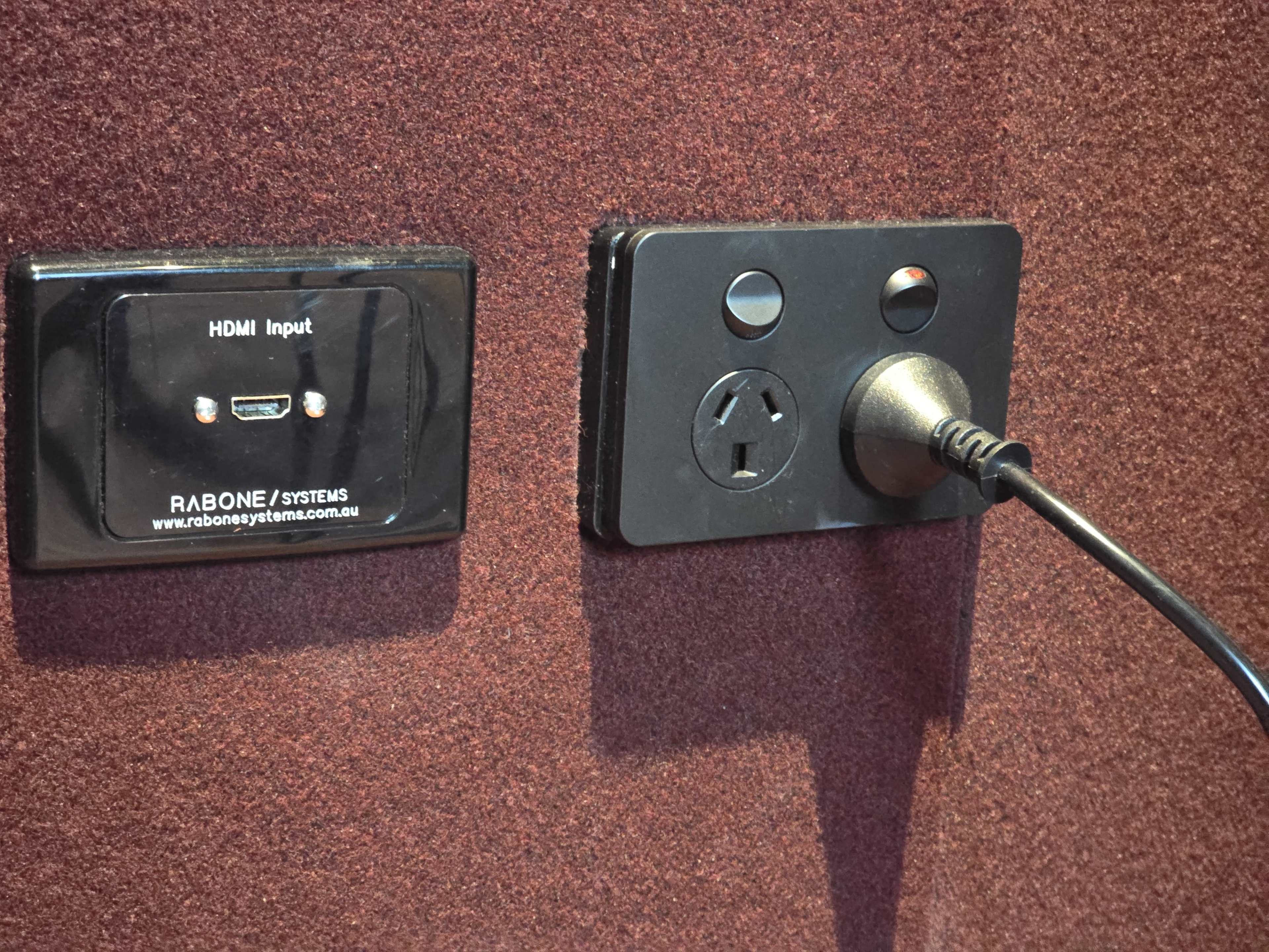 The image shows a wall plate with an HDMI input and a power outlet, accompanied by a plugged-in power cord.