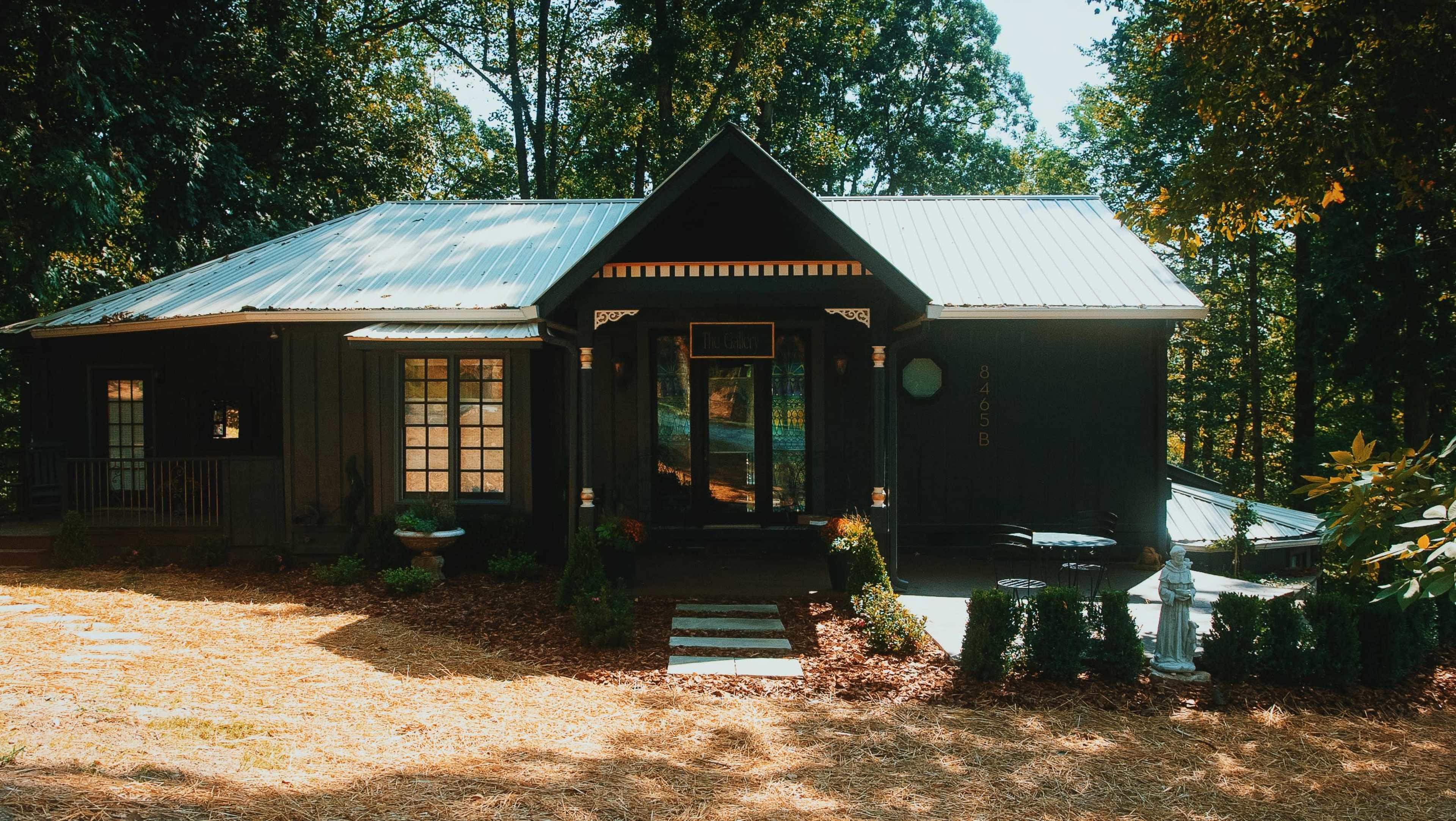 A dark-colored, modern house with a metal roof and surrounded by trees.