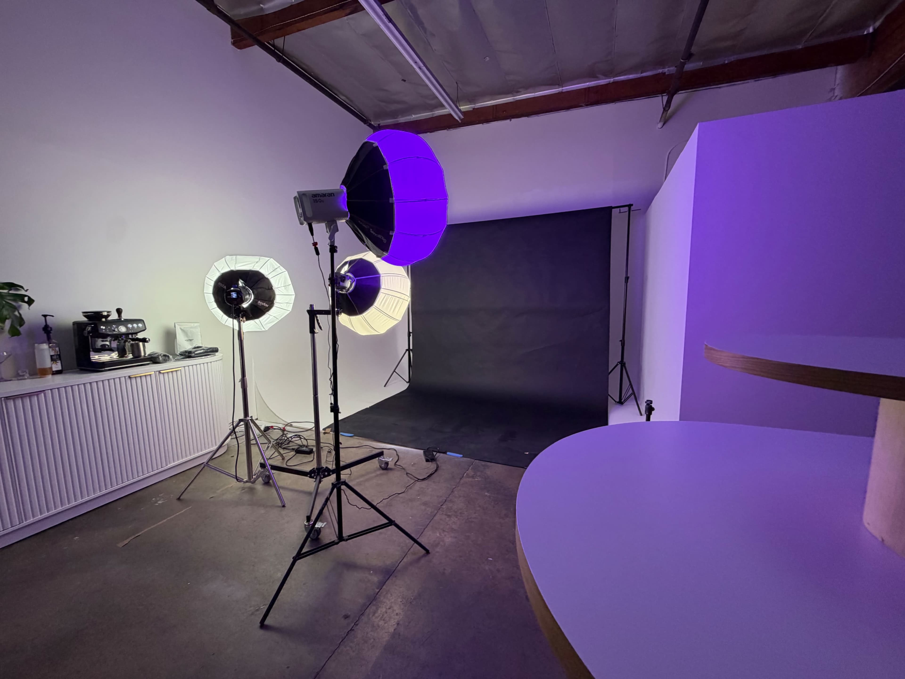 The image shows a photography studio setup featuring three lighting units, a black backdrop, and a white counter in the foreground.