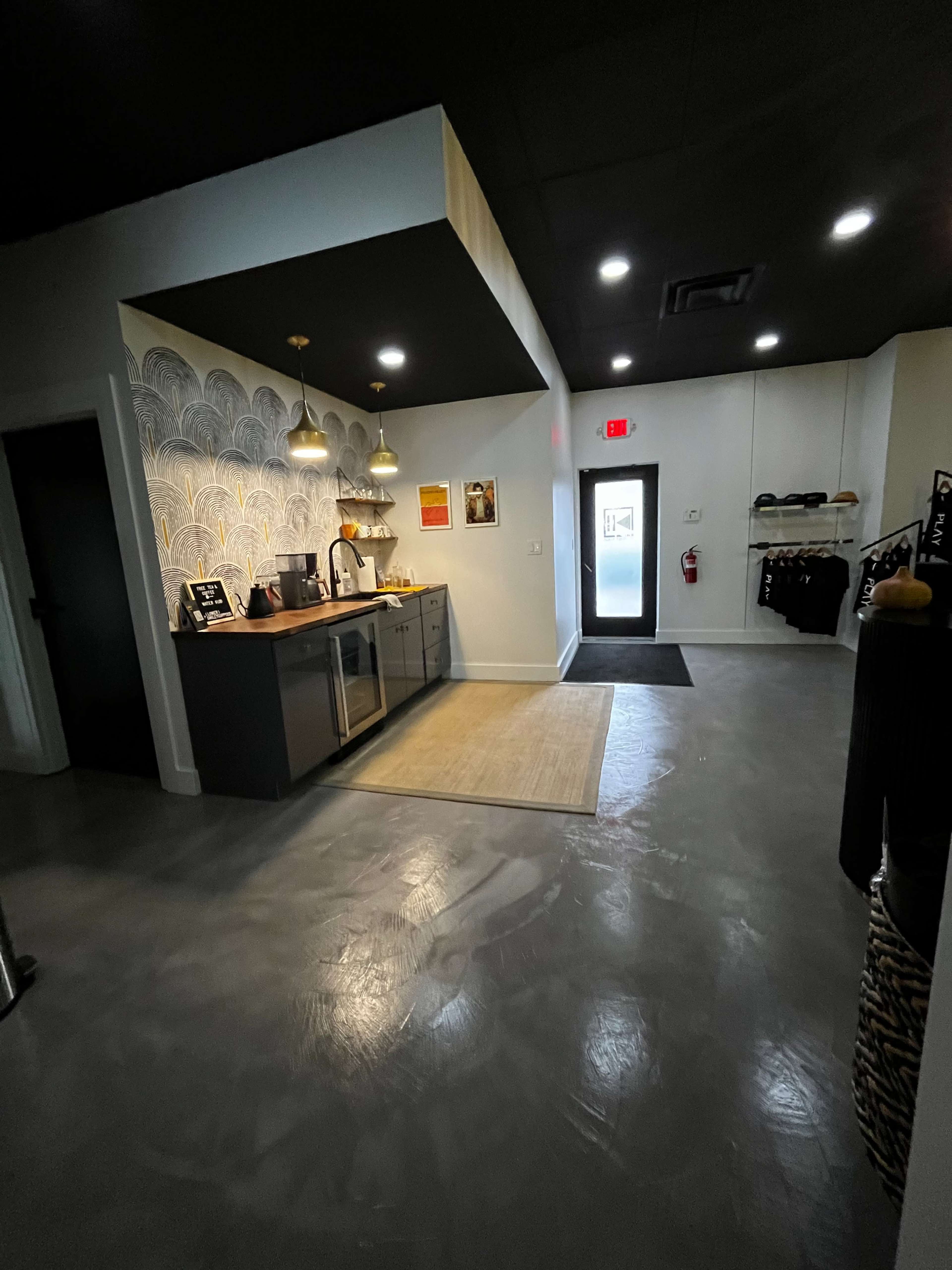 The image shows a modern kitchenette area with gray cabinets, a countertop, and decorative wall patterns, leading to an entry door with a doormat.