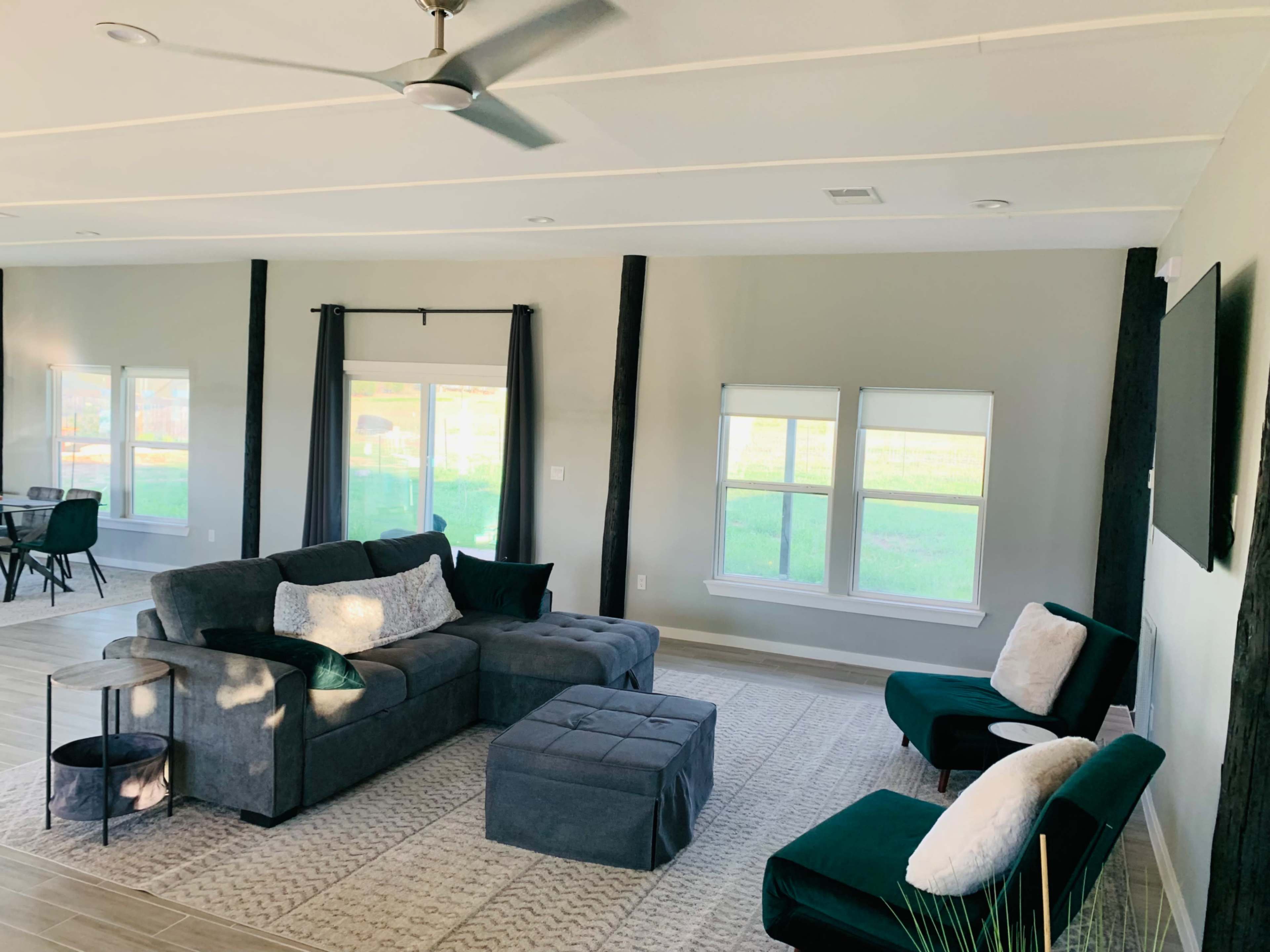 The image shows a modern living room featuring a gray sectional sofa, two armchairs, a small side table, and large windows letting in natural light.