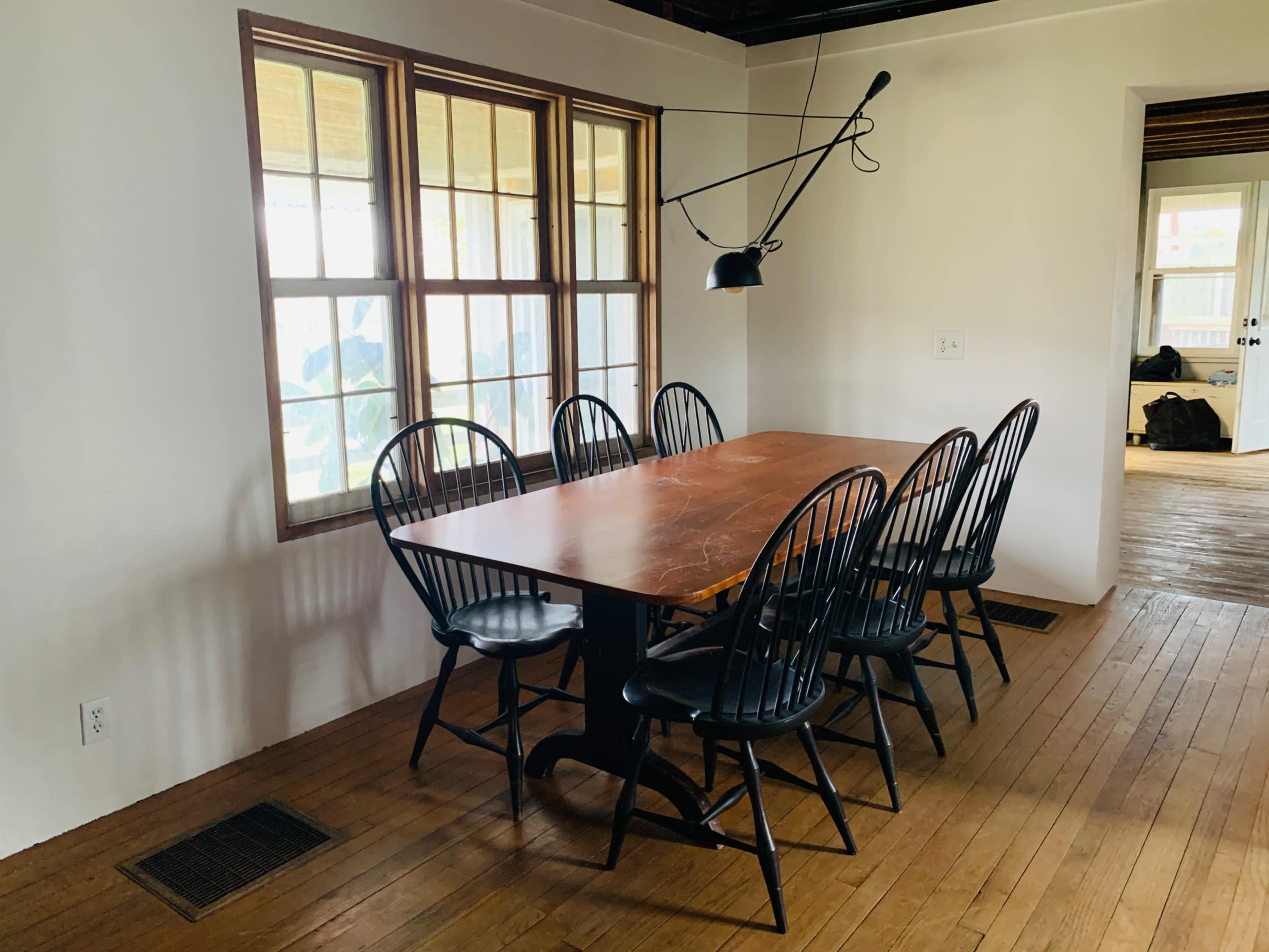 A large wooden dining table is surrounded by eight black chairs, with a wall of windows providing natural light.